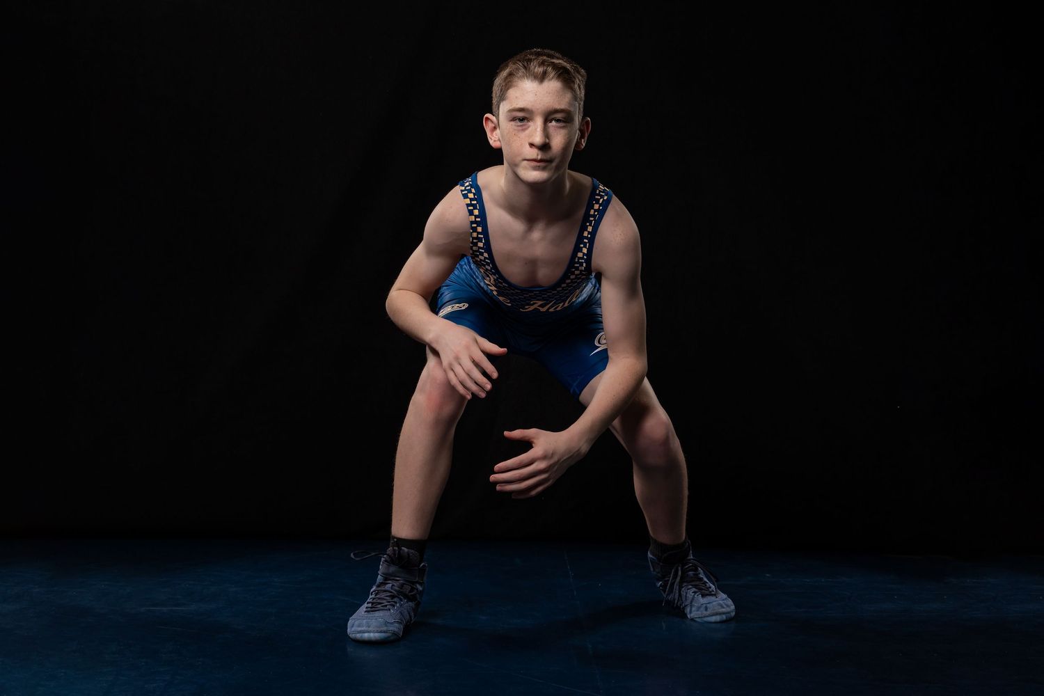 Athletic person in workout attire crouches in ready position against dark background during fitness photoshoot.