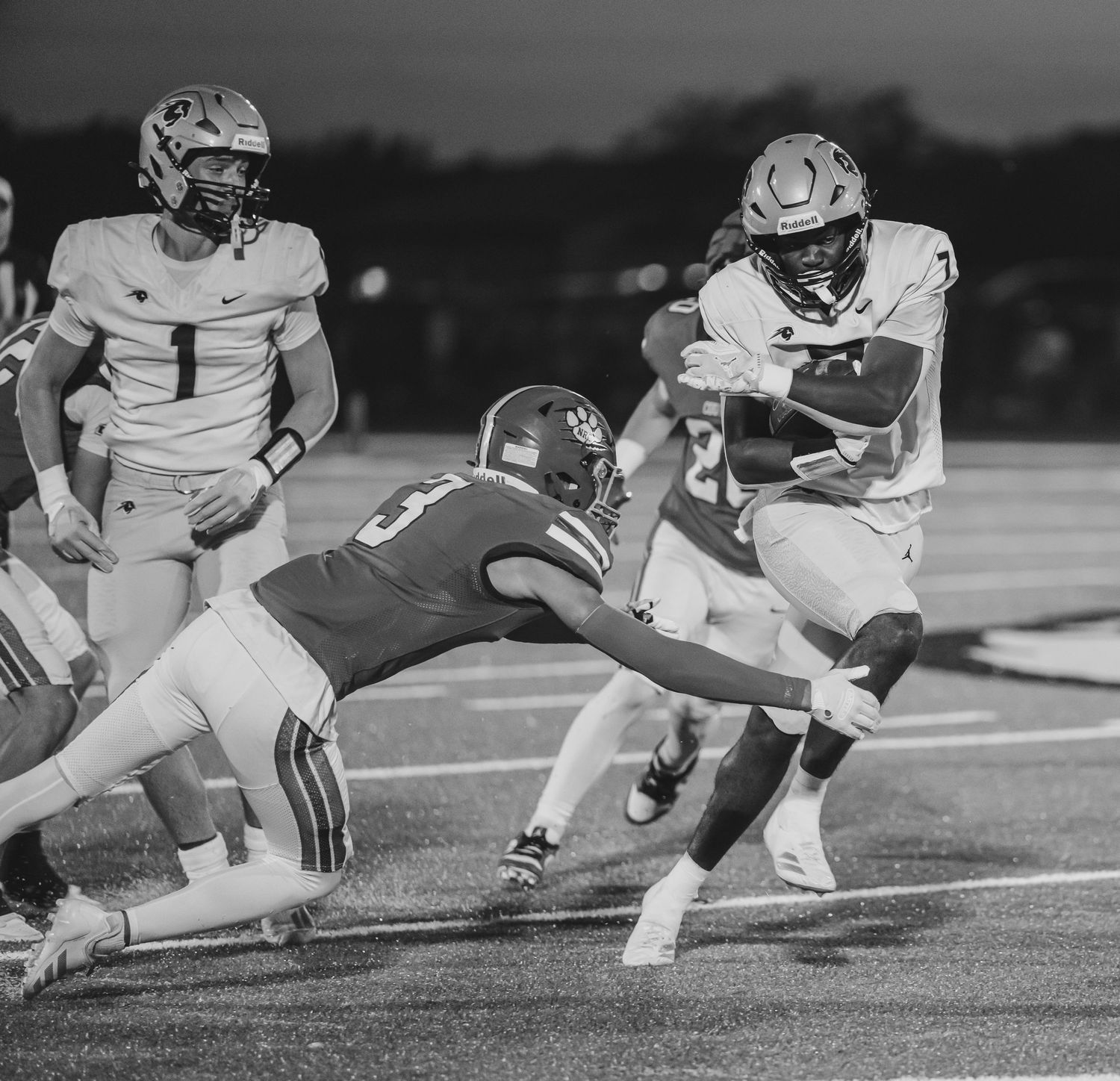 Black and white sequence of football players diving and tackling during a game on the field.