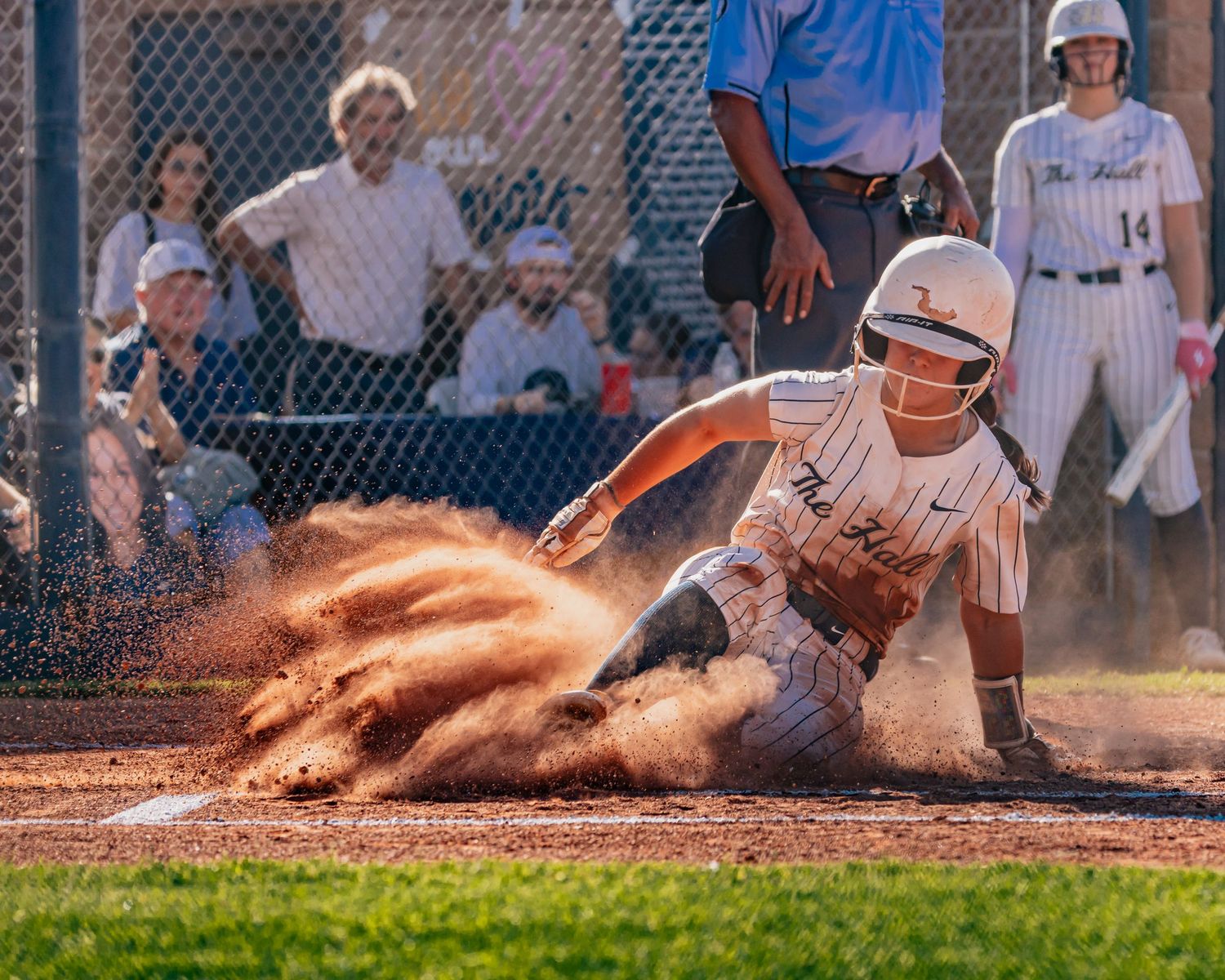 softball player slides into home plate creating a dramatic cloud of orange dirt during an intense game moment.