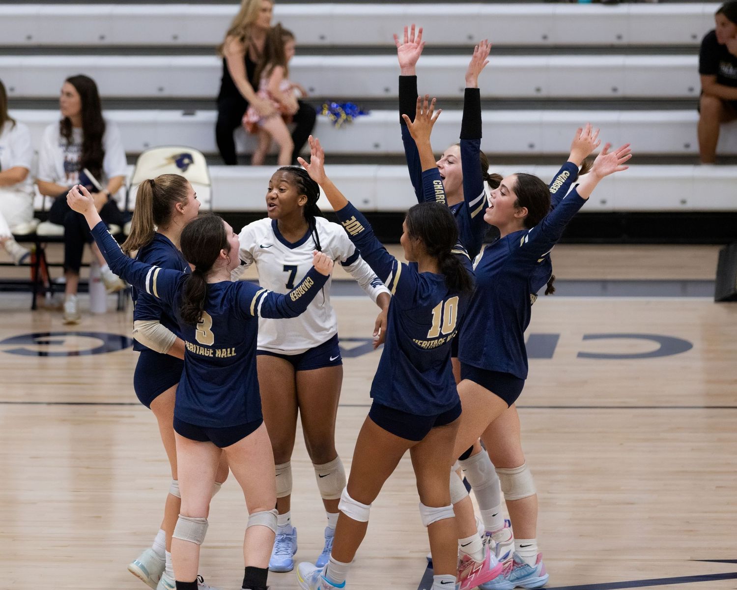Volleyball players in navy blue uniforms celebrate on the court during a match.