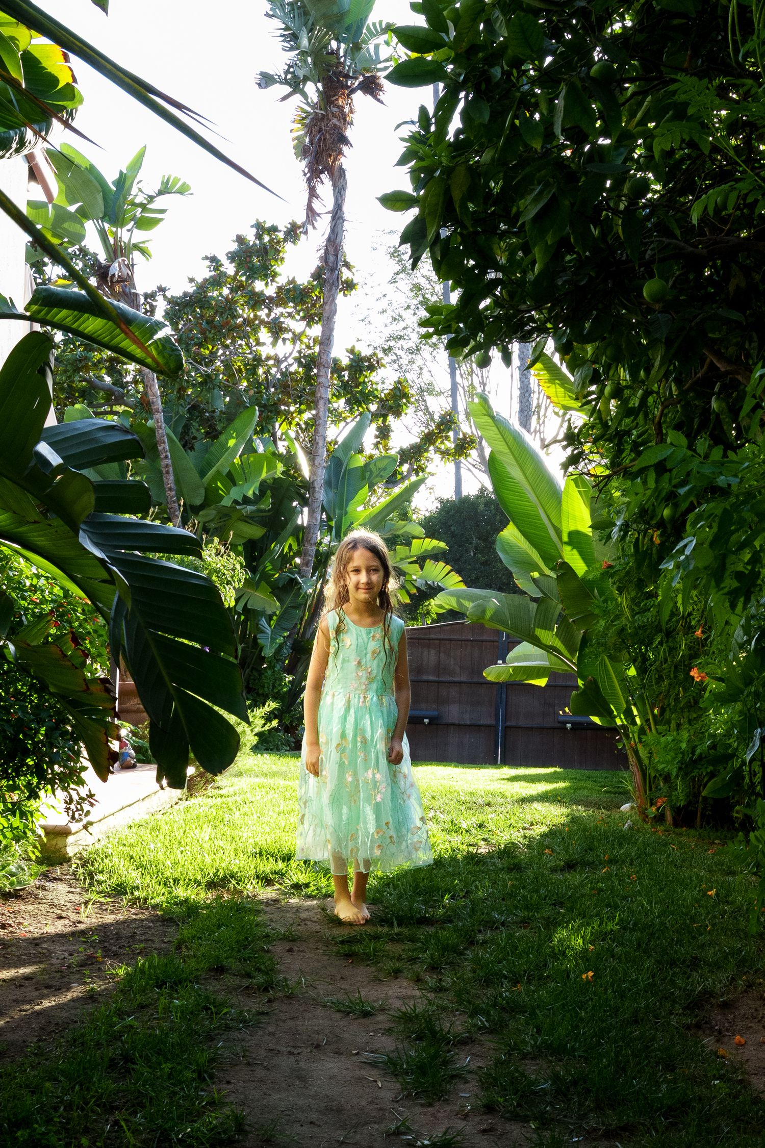 a natural photo of a girl in her backyard surrounded by lush greenery and natural light