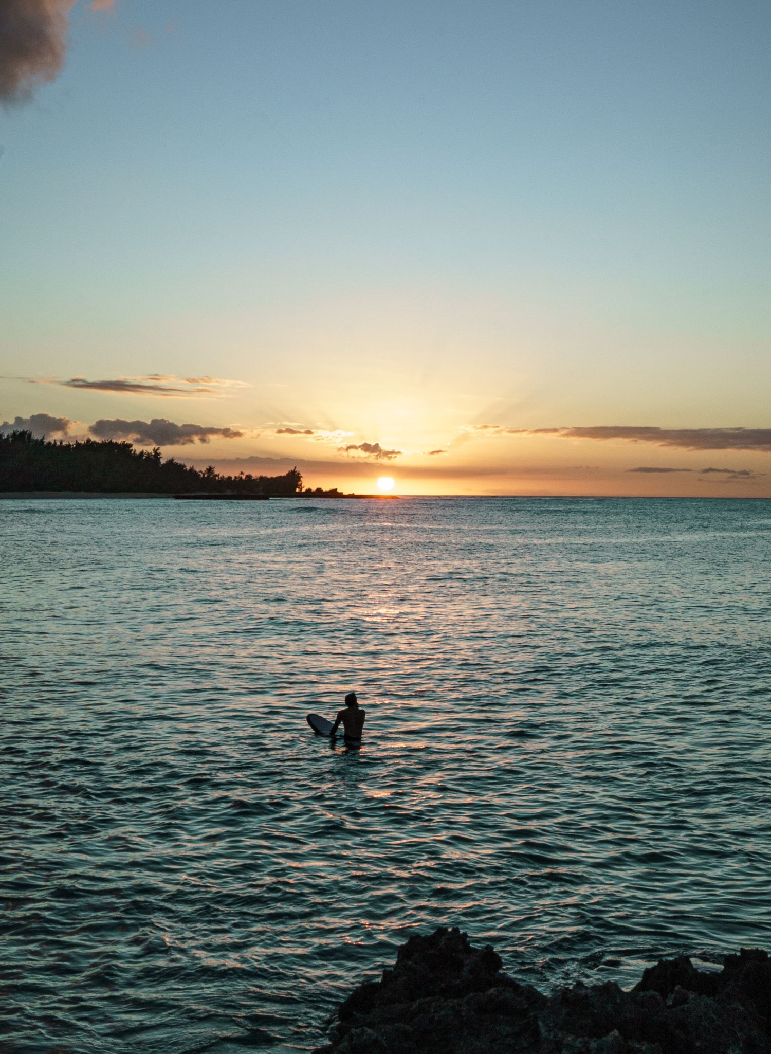 The silhouette of a single surfer sitting on a surfboard in the ocean at sunset