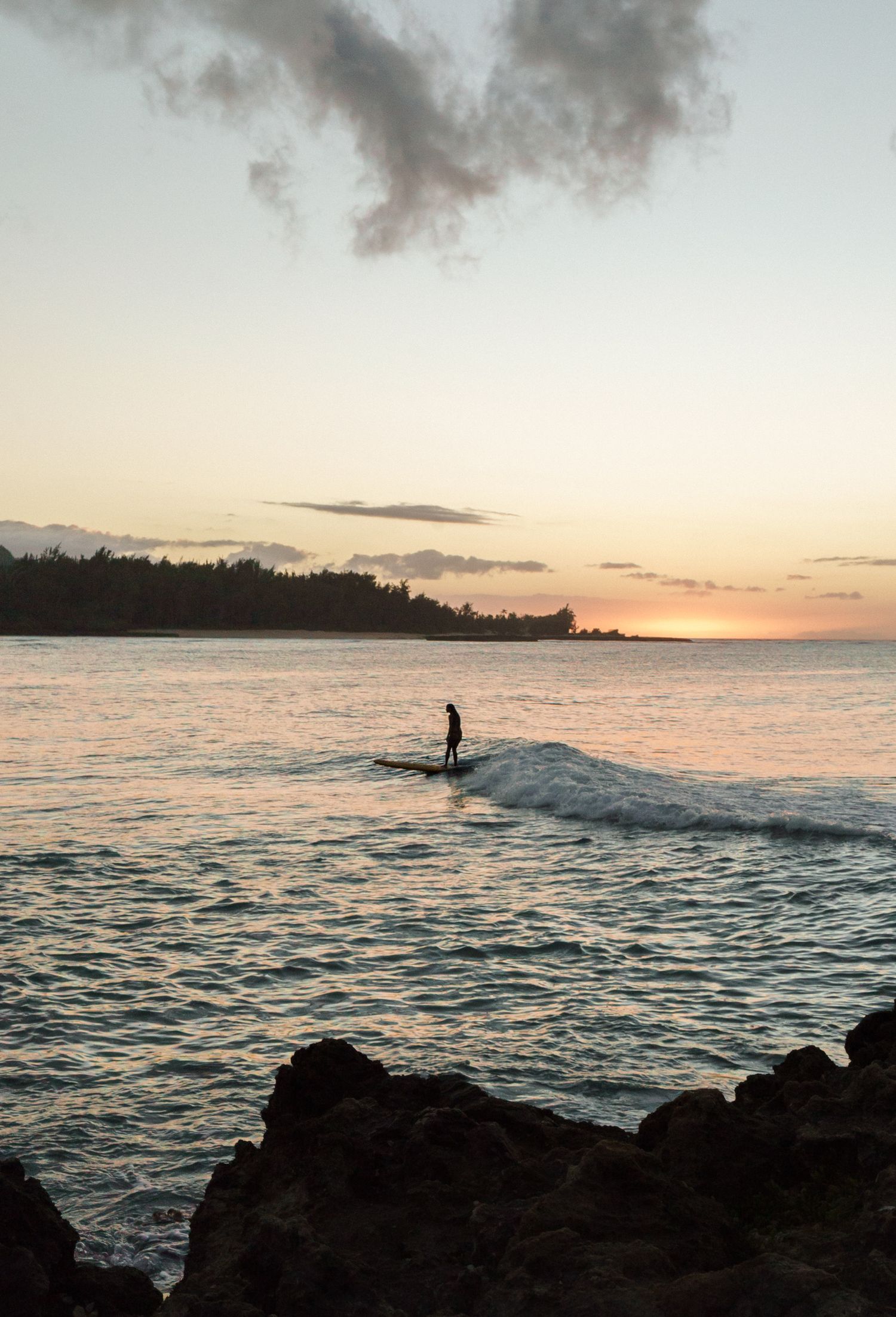 a silhouette of a single surfer riding a wave at sunset in Hawaii