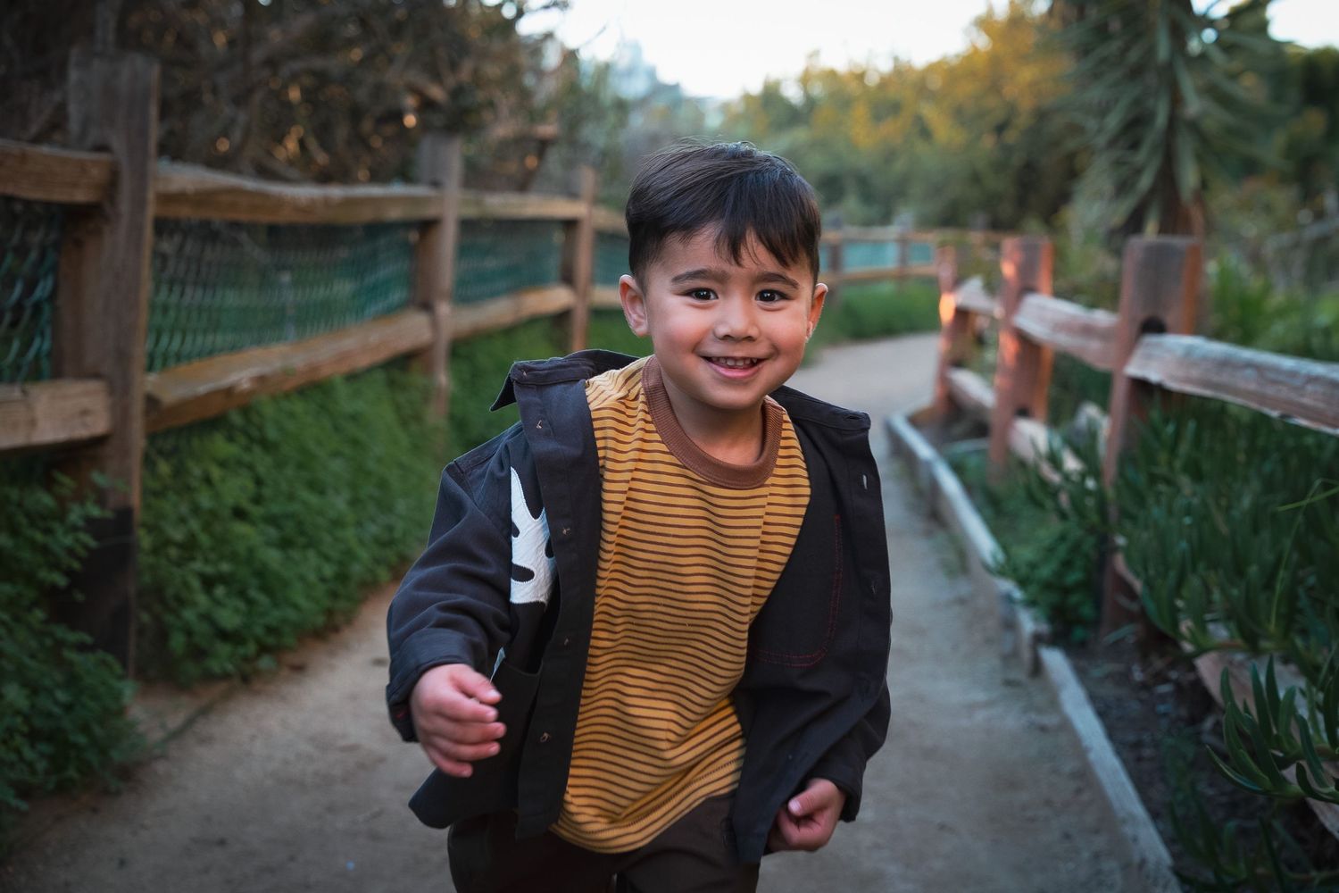 a toddler running down a path a smiling at the camera