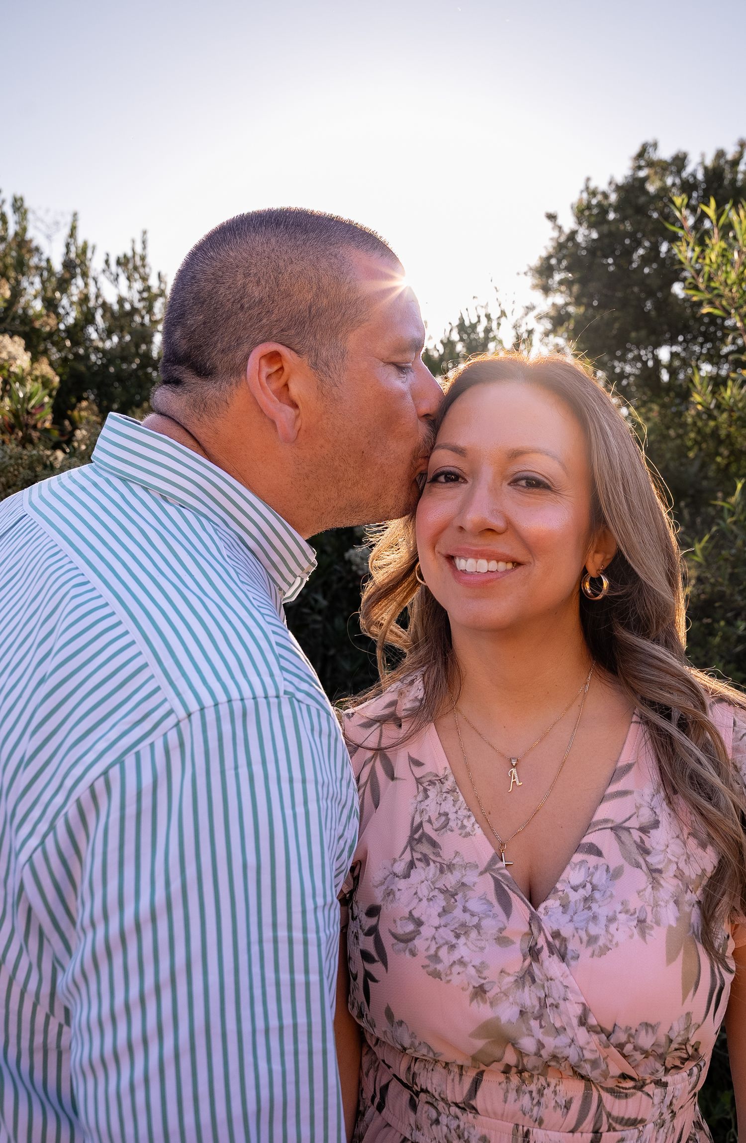 a picture of a husband in profile kissing his wife's forehead during golden hour with a starburst in between them