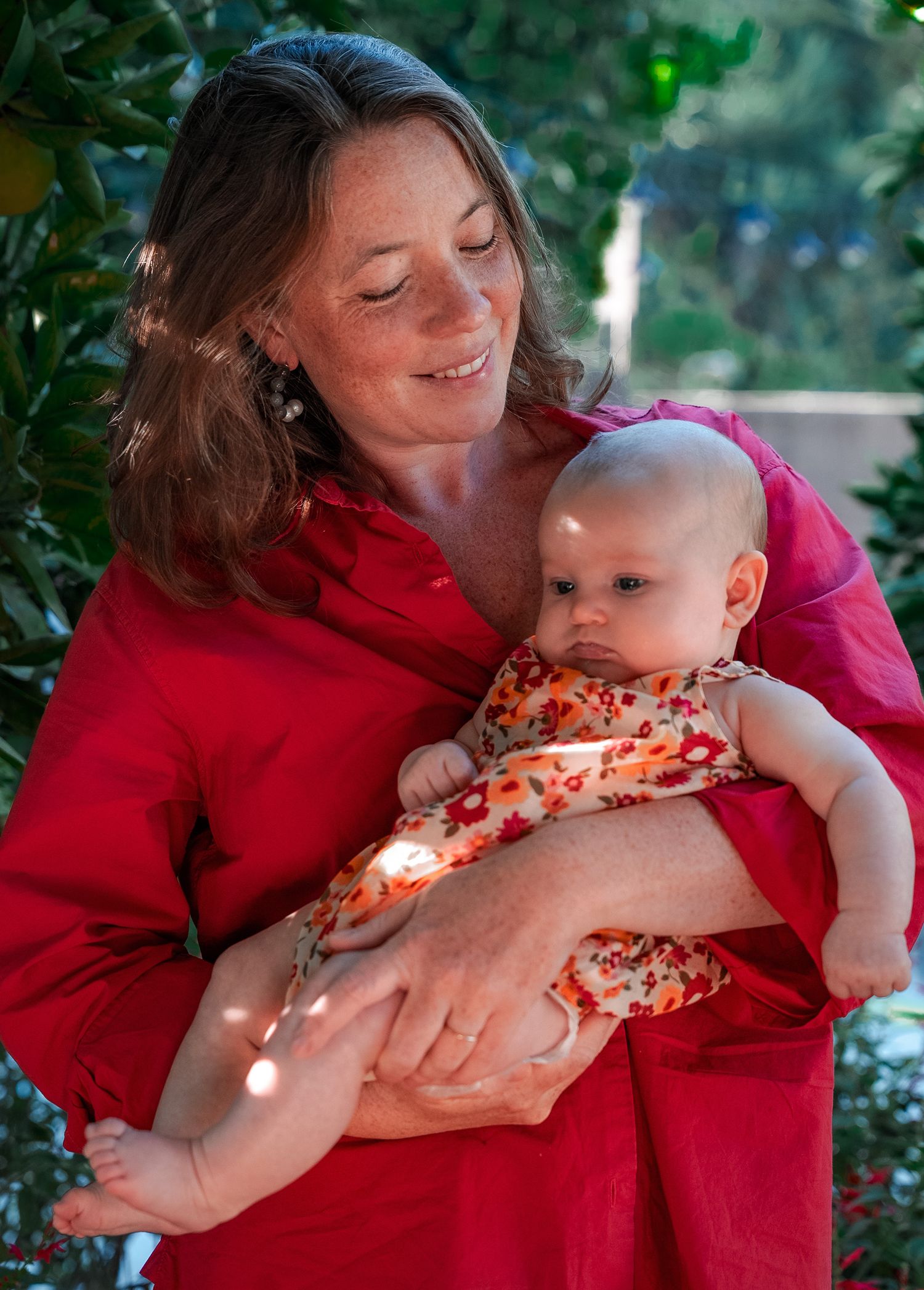 an intimate photo of a mother holding her baby daughter in front of some greenery