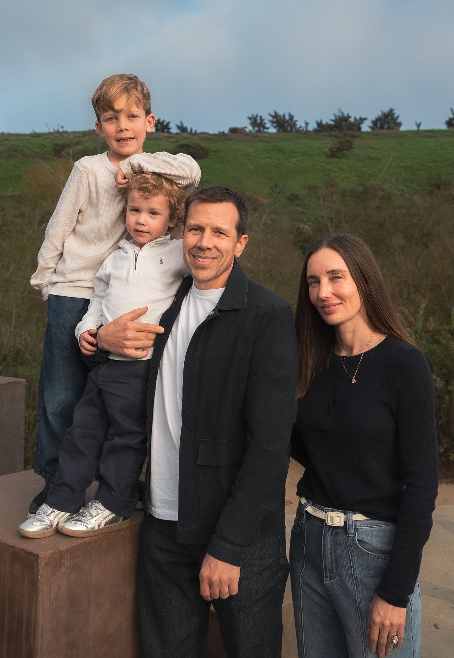 a natural family portrait of a family of four smiling at the camera at the park