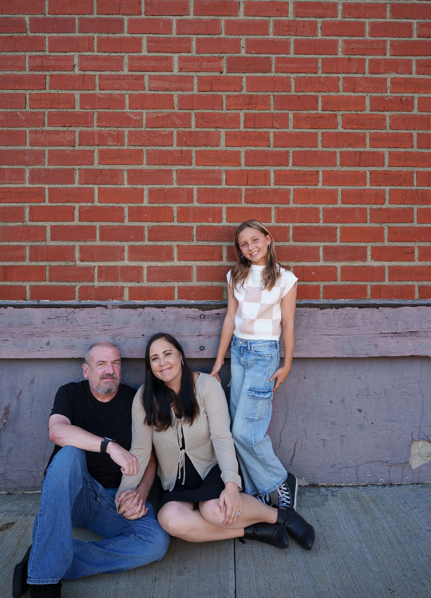 A family of three leaning against a brick wall and looking at the camera
