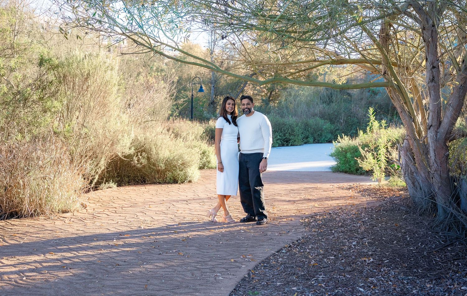 a couple dressed up in white under a large tree