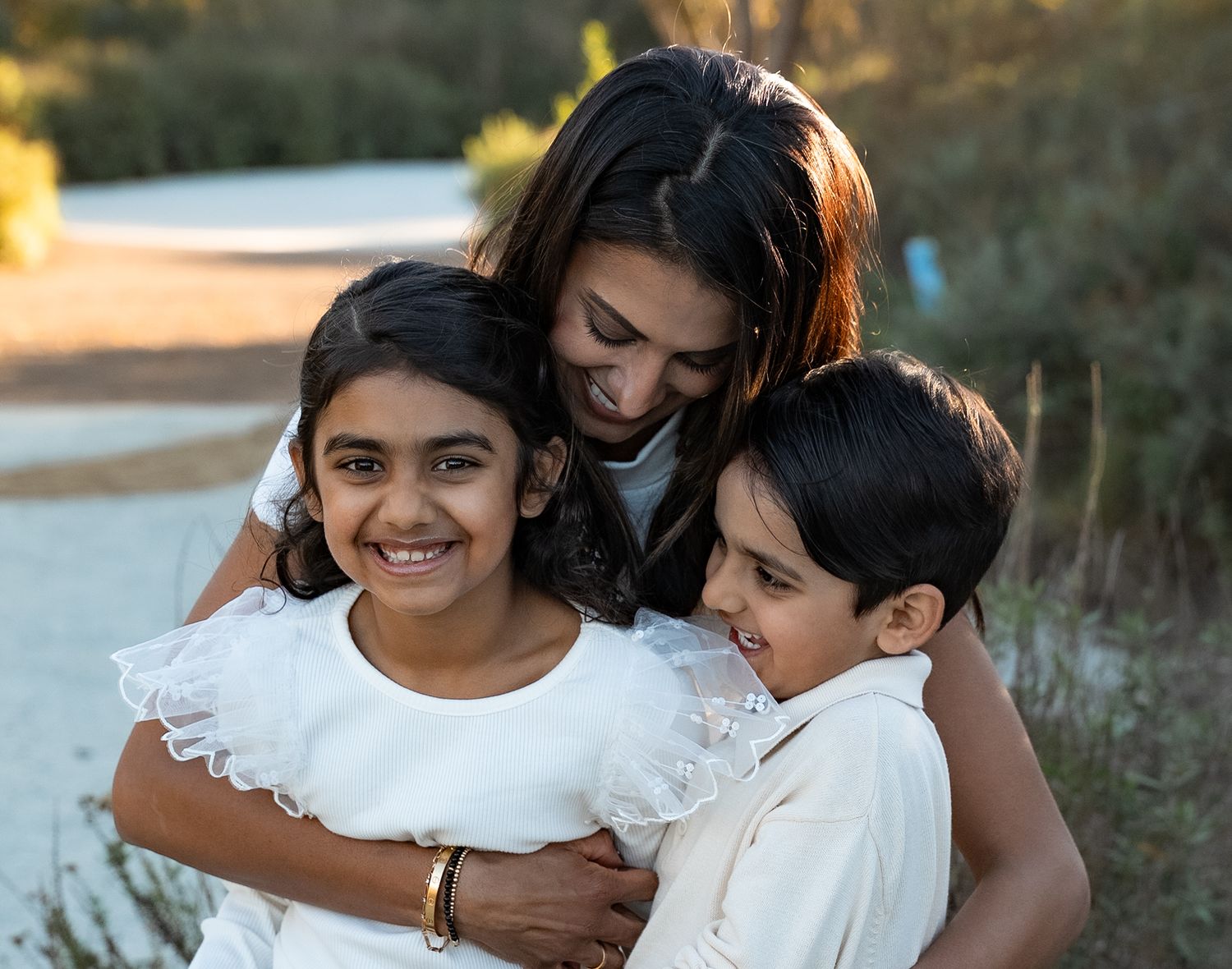 a mother hugs her two young children at the park