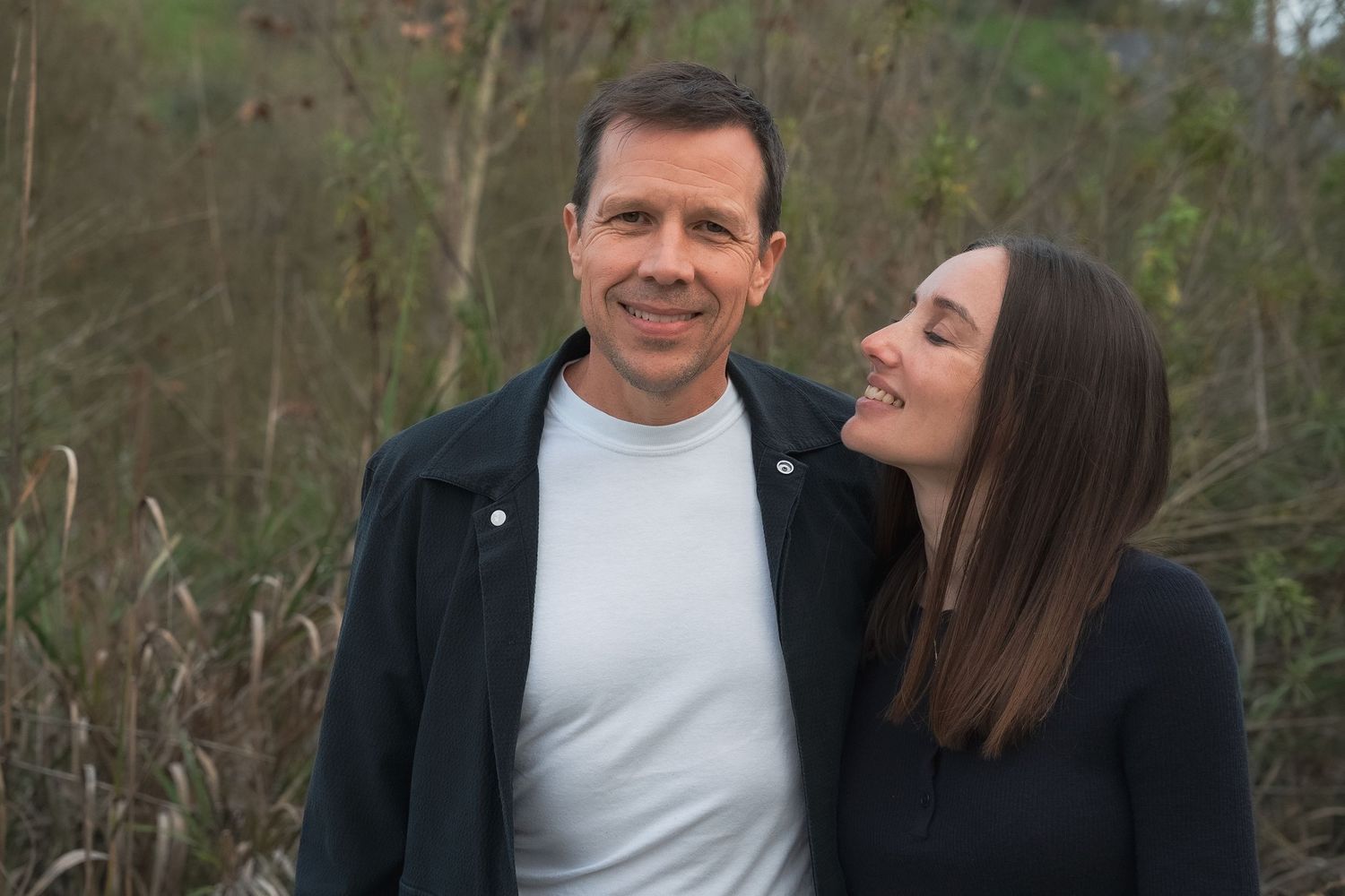 a couples photo at a park of a wife looking lovingly at her husband while he smiles at the camera