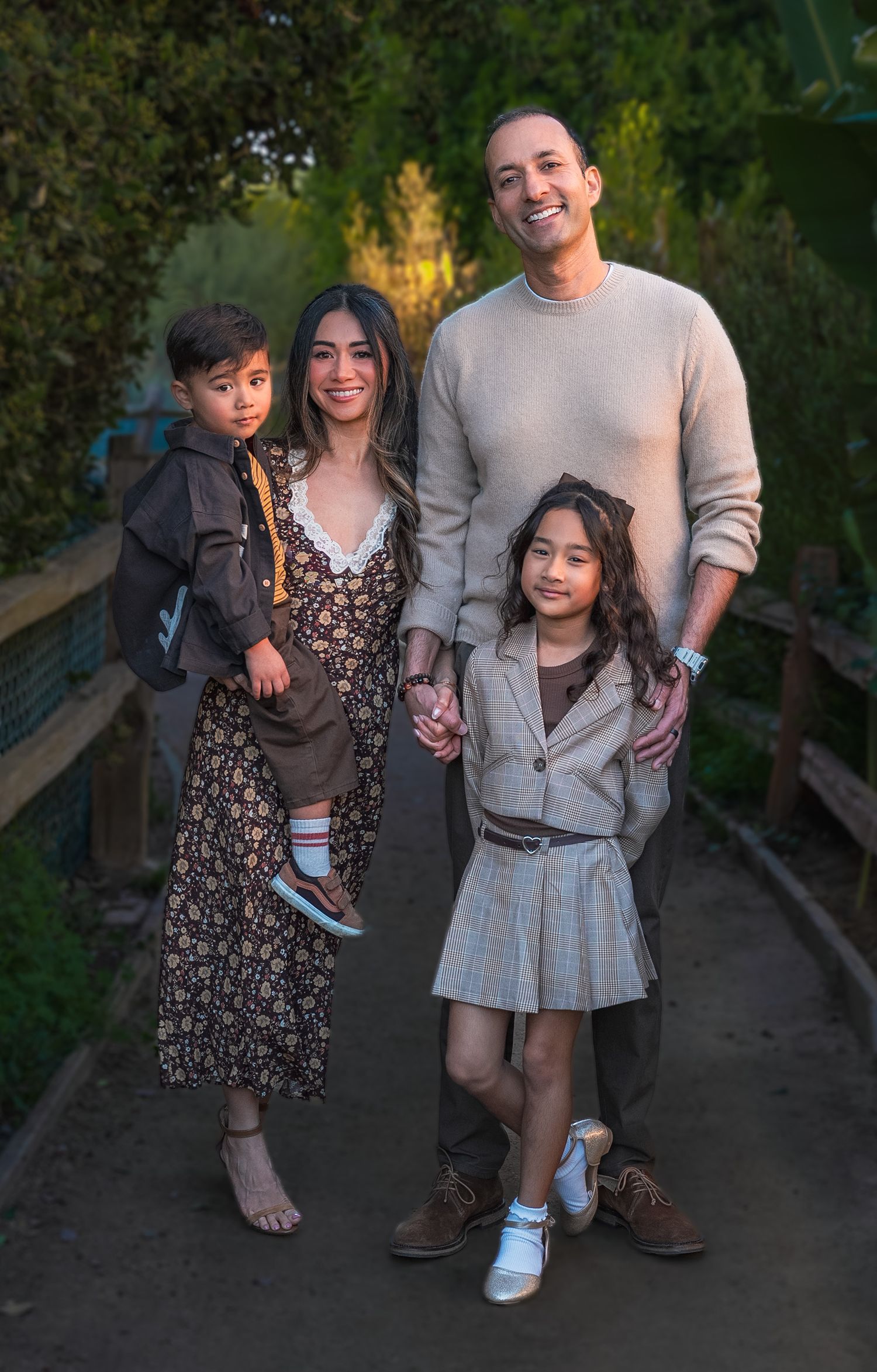 a family portrait of four on a lush path at sunset where they all are smiling at the camera