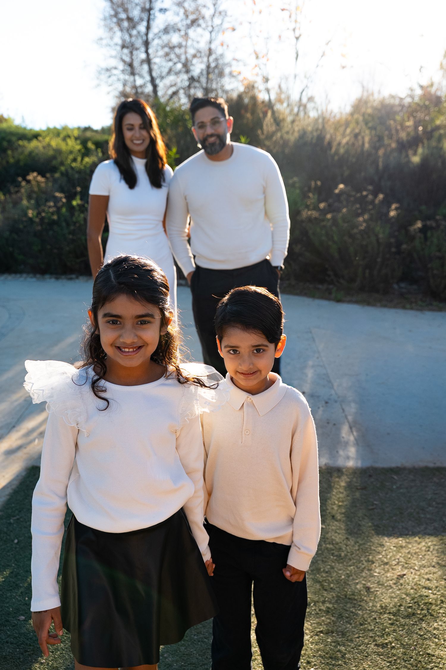 a natural portrait of a family of four where the brother and sister are in focus in the foreground and the parents watch them from behind