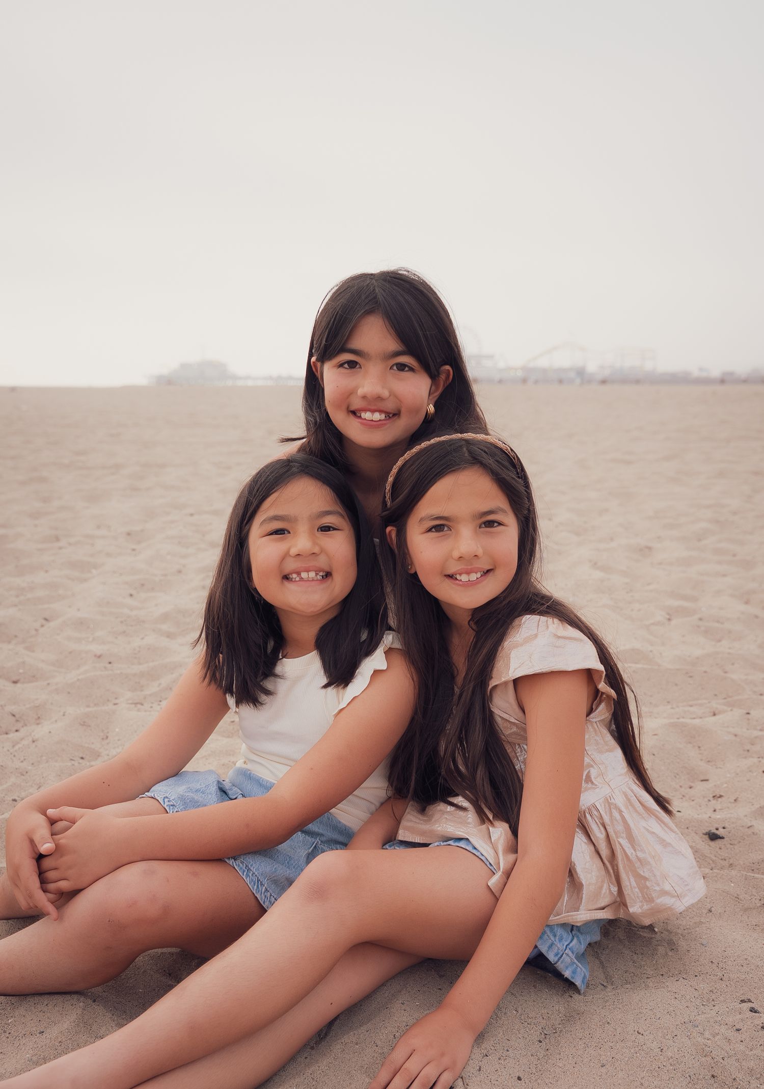 a relaxed portrait of three sisters sitting in the sand and smiling at the camera