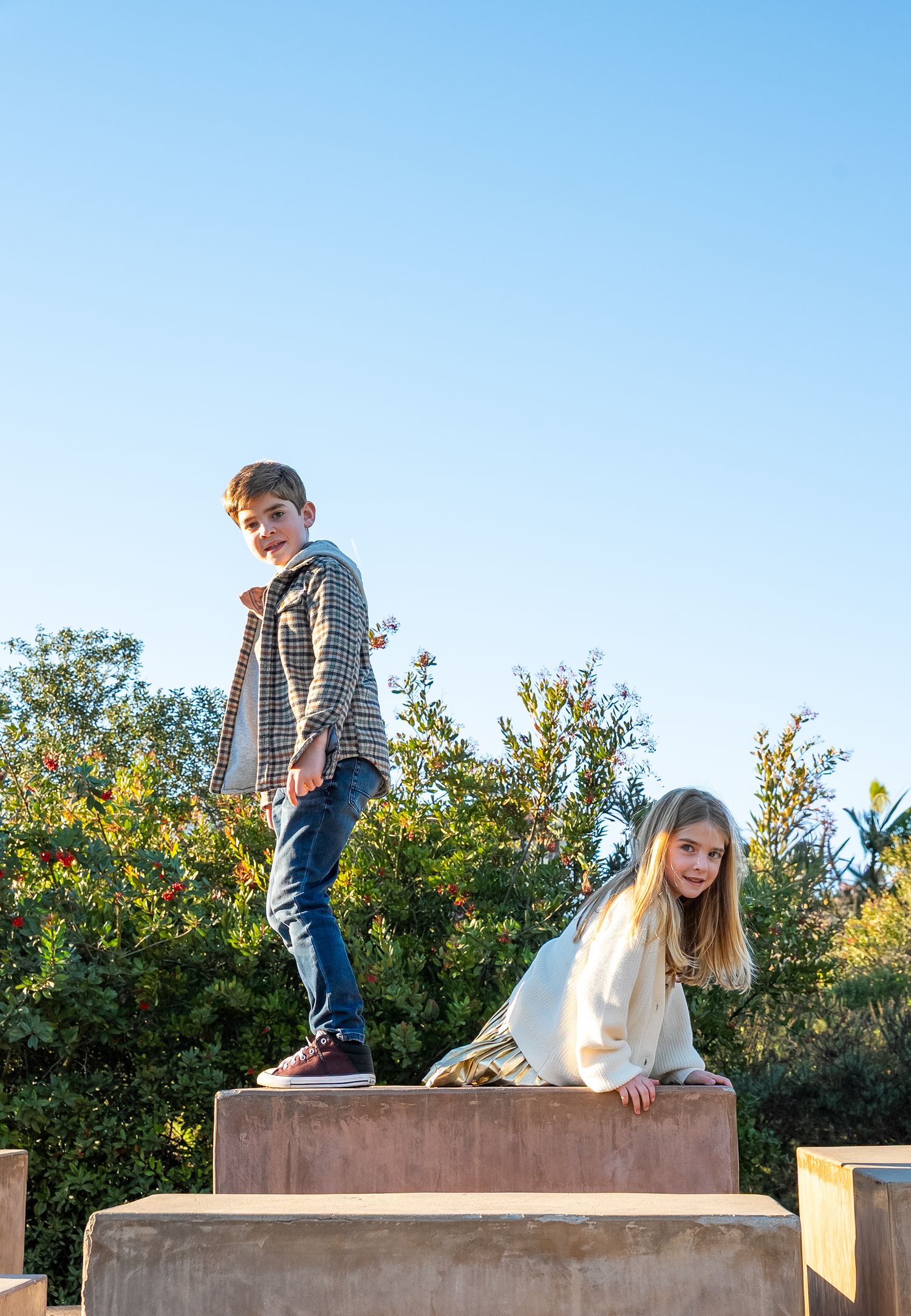 a candid photo of a brother and sister climbing on some tall terra cotta blocks looking down at the camera
