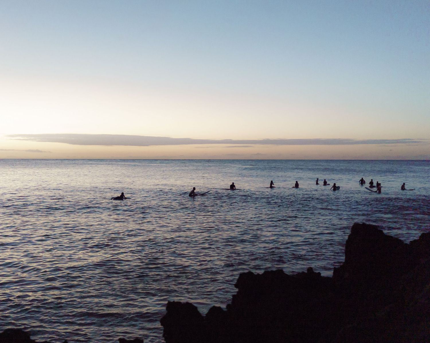 a sunset photo of the ocean dotted with surfers in the distance and cliffs