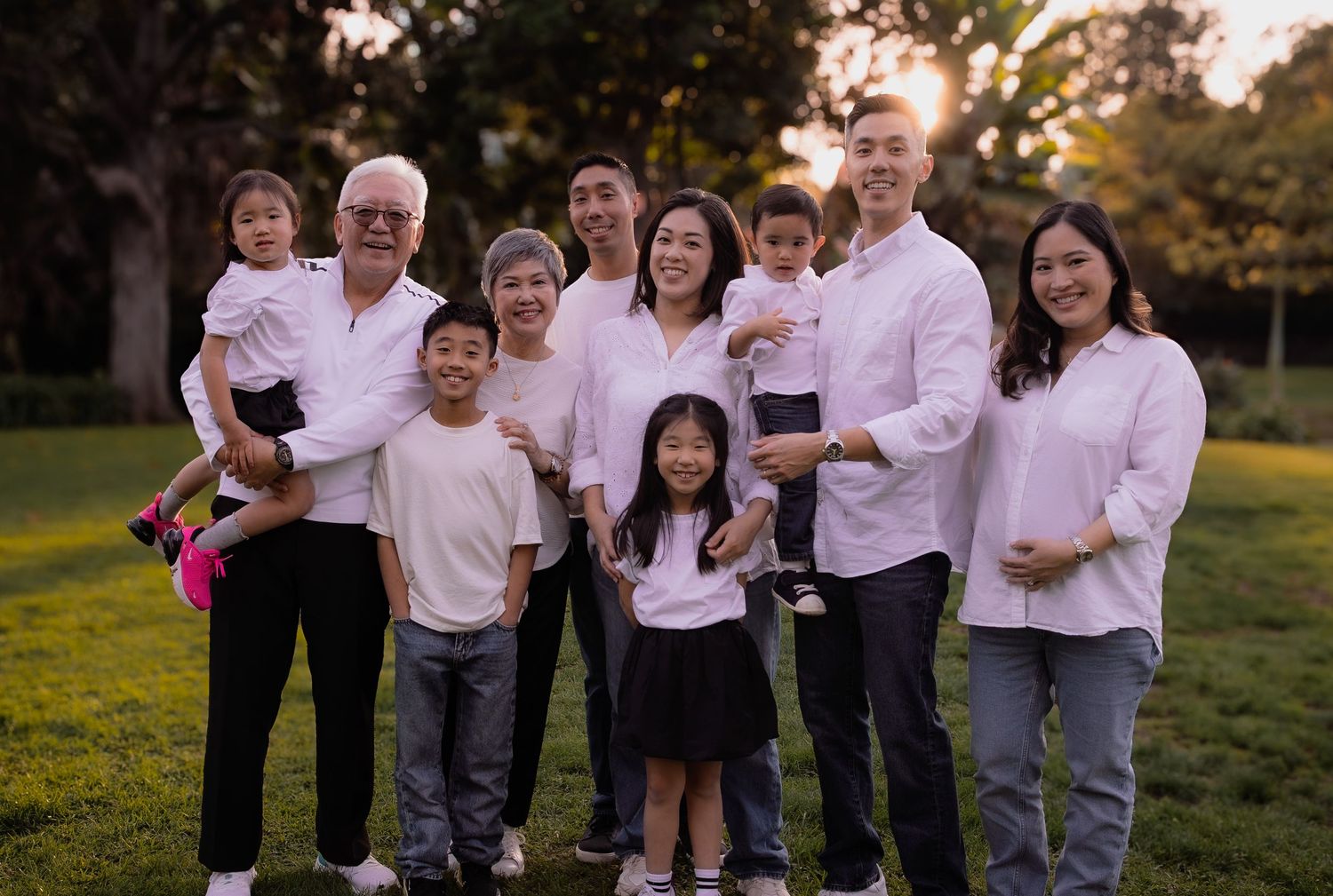 a relaxed portrait of an extended family of three generations all wearing white at a park during golden hour