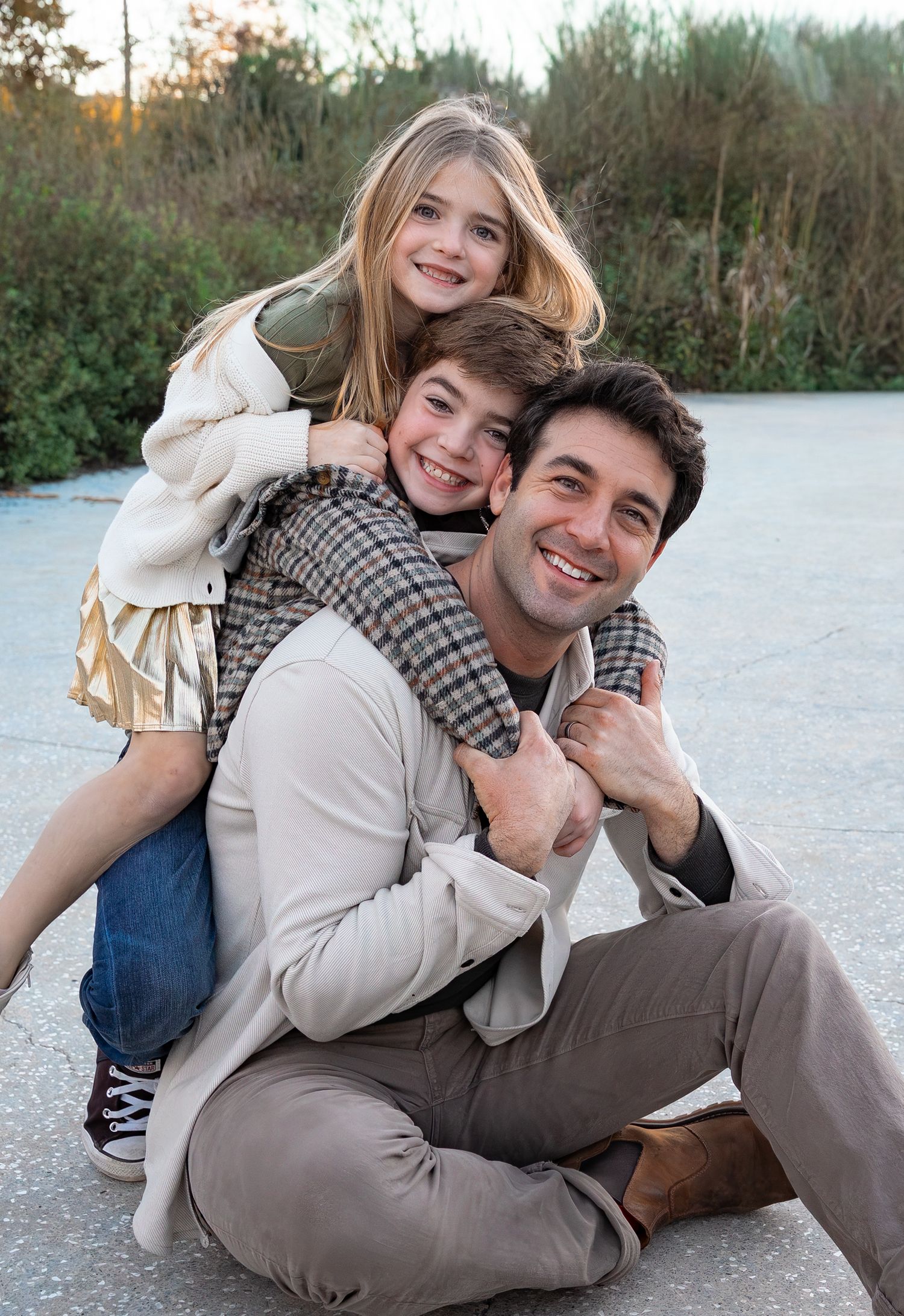 a father and his two children hugging his back while they all smile at the camera