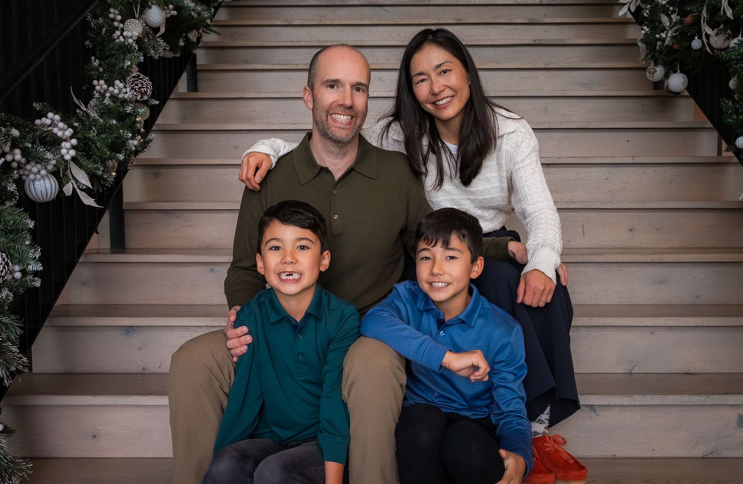 a holiday-themed photo of a family of four sitting casually on a decorated staircase