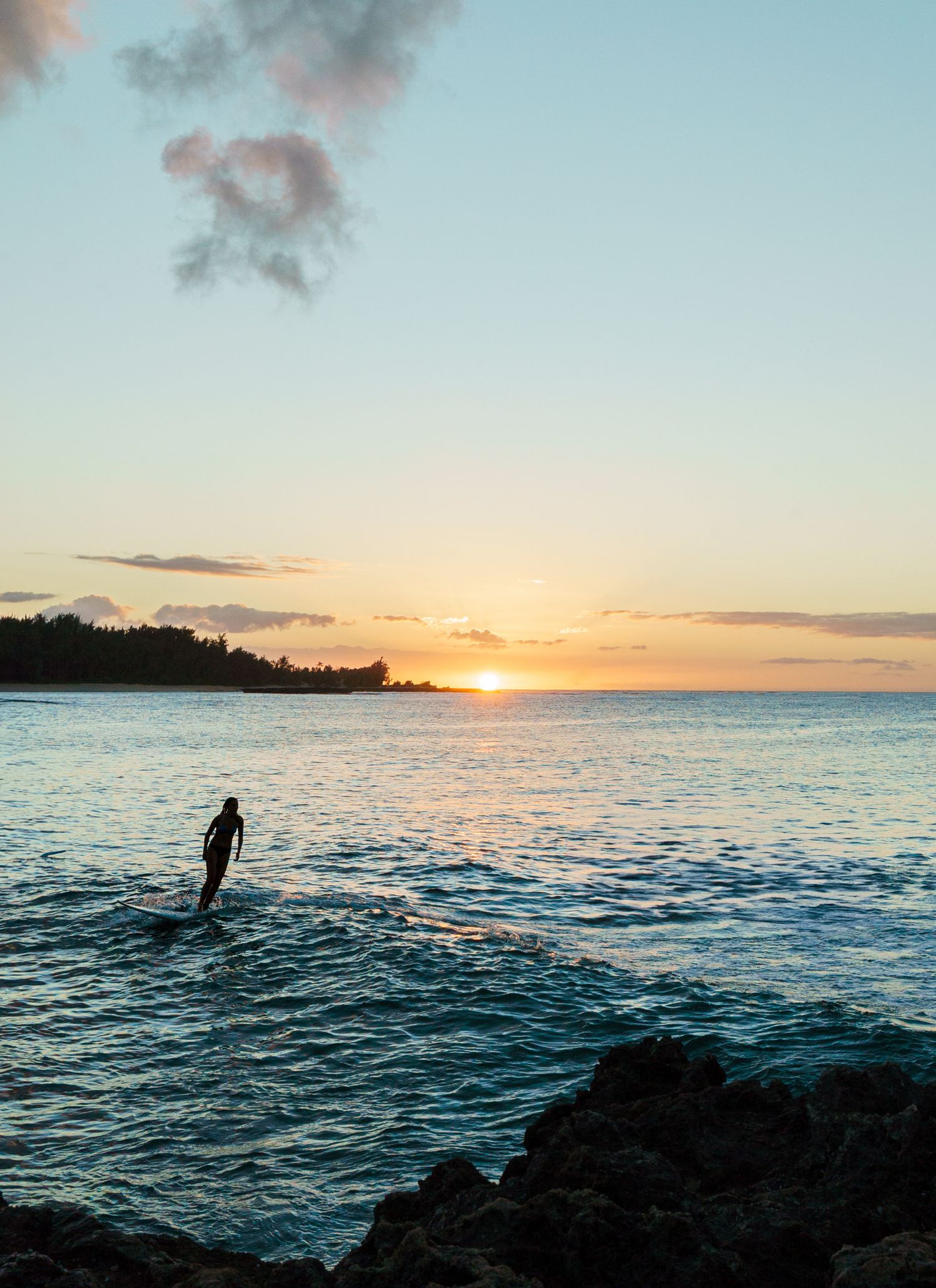A photo of a single surfer riding a wave at sunset in Hawaii