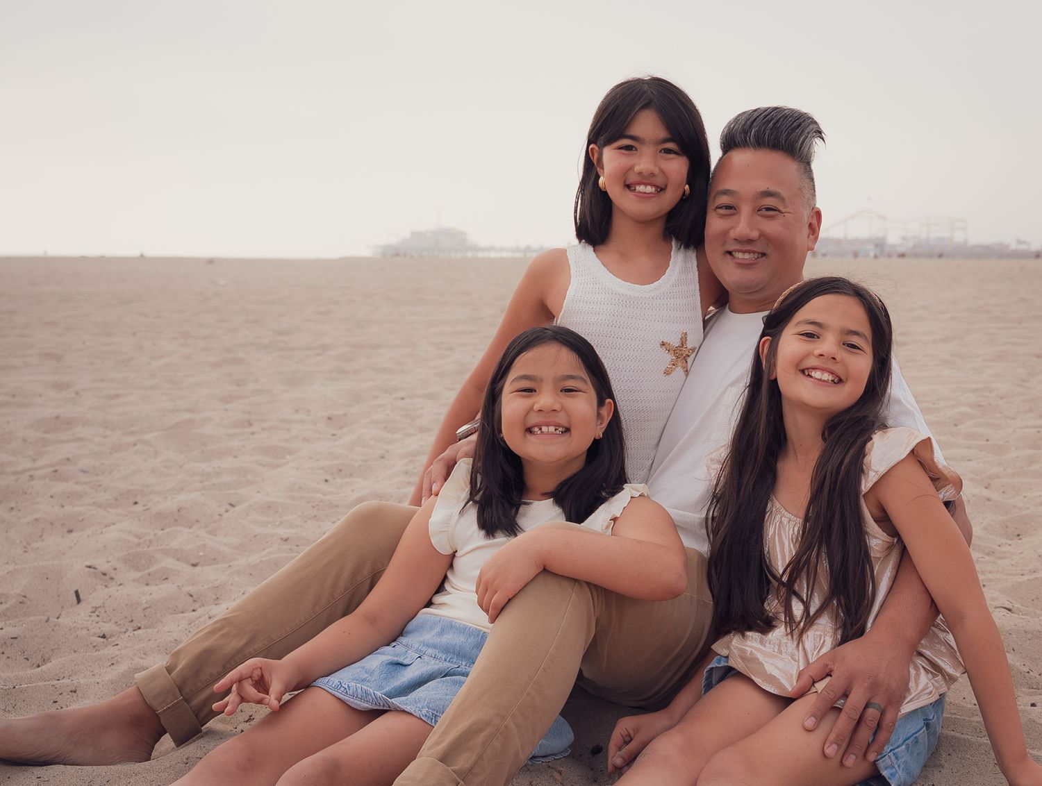 a natural relaxed portrait of a father with his three daughters sitting on the sand at the beach