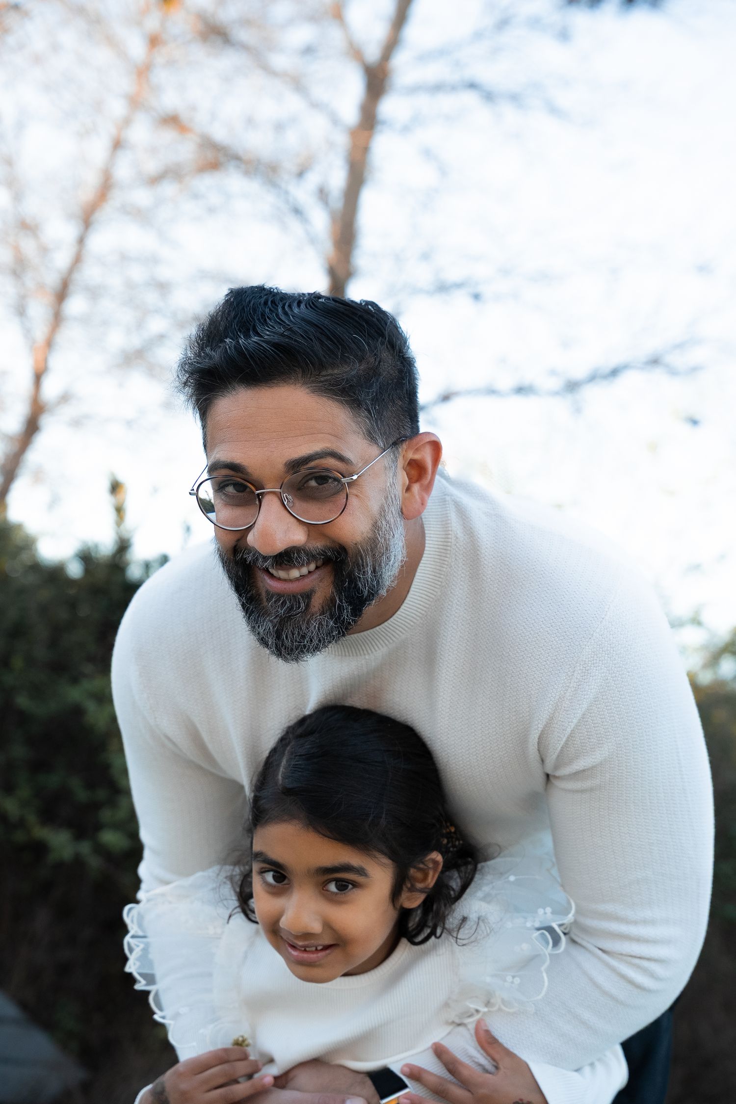 a father bends down to hug his daughter from behind dressed in white