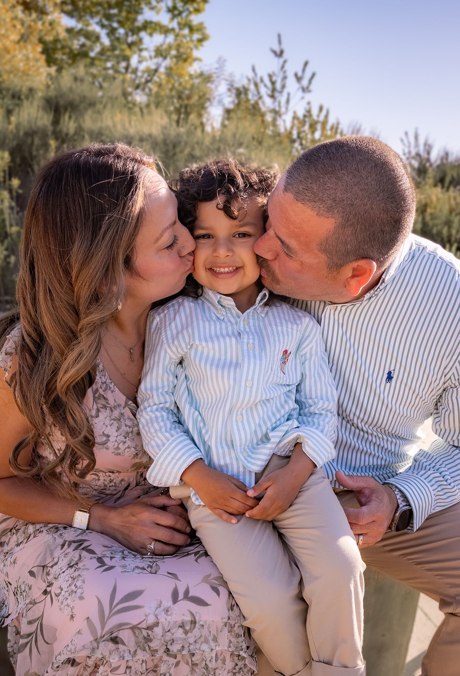 a mother and father surrounding their smiling son and each kissing him from both sides