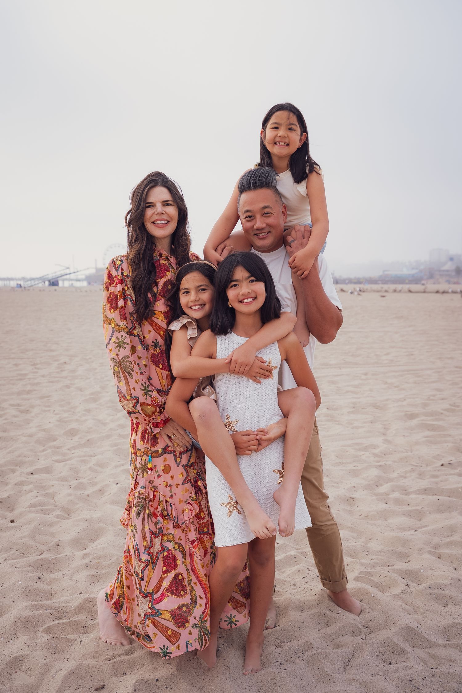 a family of five standing on the sand at the beach and smiling at the camera