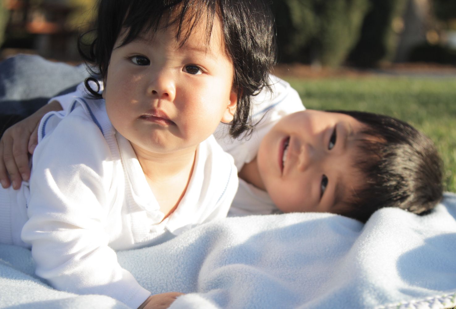 a candid shot of a toddler boy and his baby brother relaxing on a blanket at the park