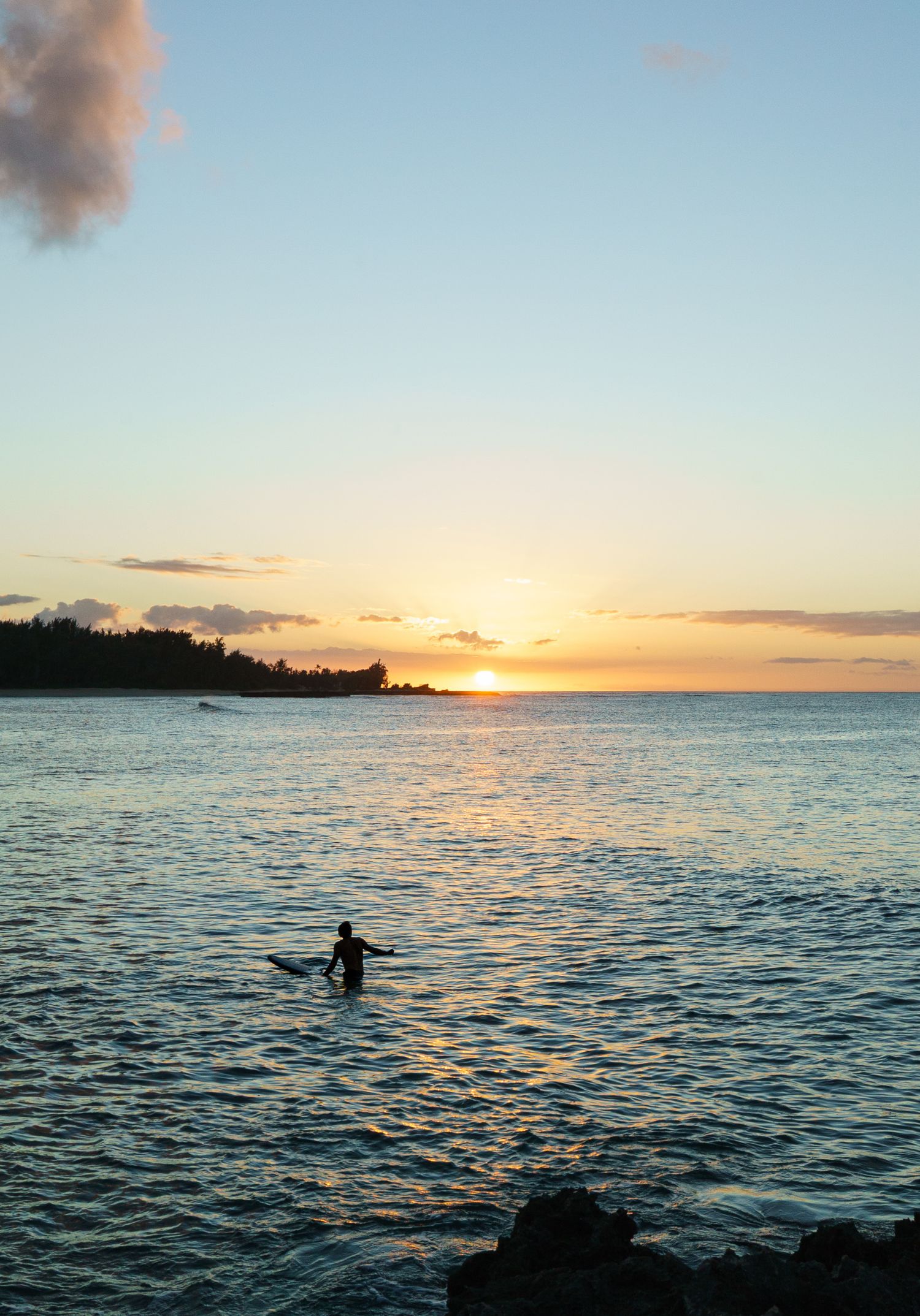 The setting sun over the ocean at the north shore of Oahu with a single surfer waiting for a wave