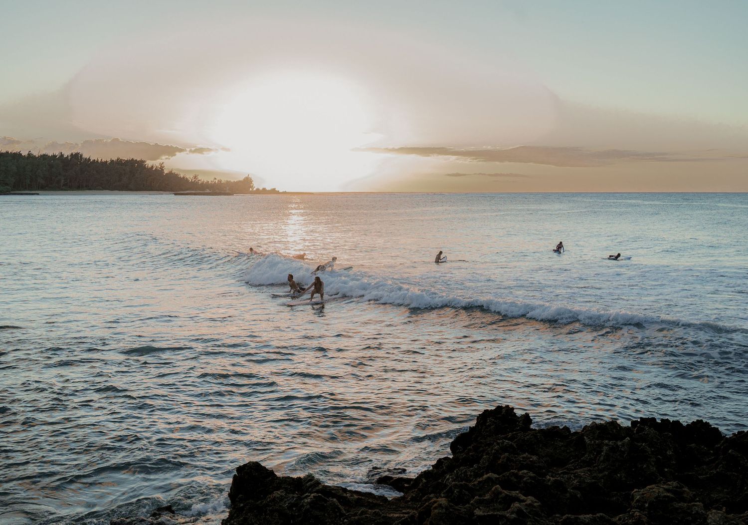 a photo of a hawaiian sunset over the ocean with the silhouette of several surfers riding a wave