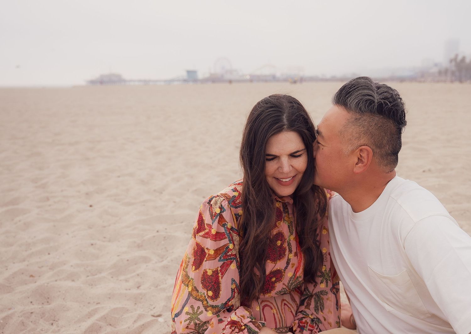 a sweet photo of a couple cuddling on santa monica beach at sunset
