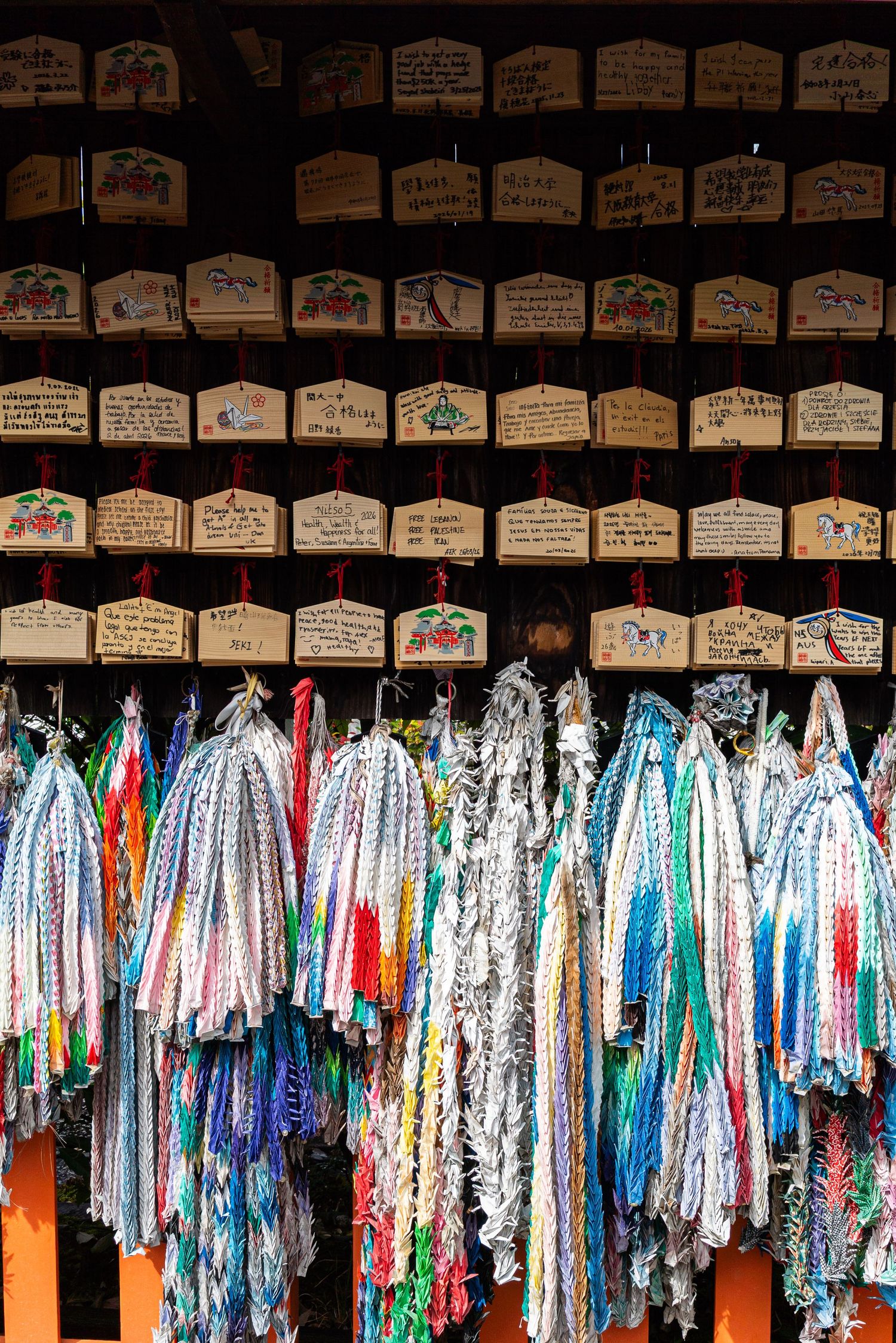traveler well-wishes at a temple in Tokyo where the upper half of the photo is wooden messages while the bottom half are colorful fabric
