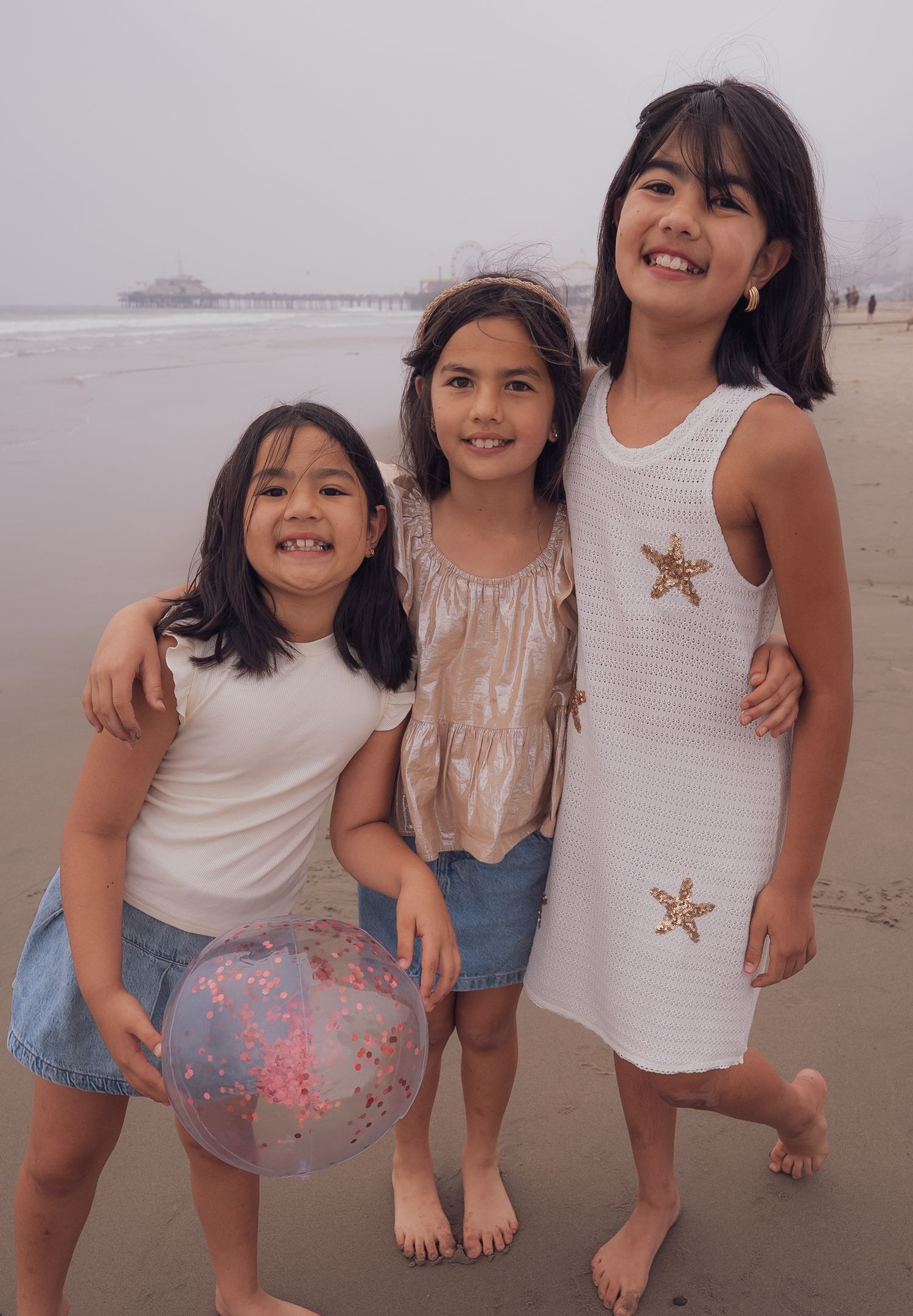 a smiling portrait of three sisters holding a beach ball at the beach