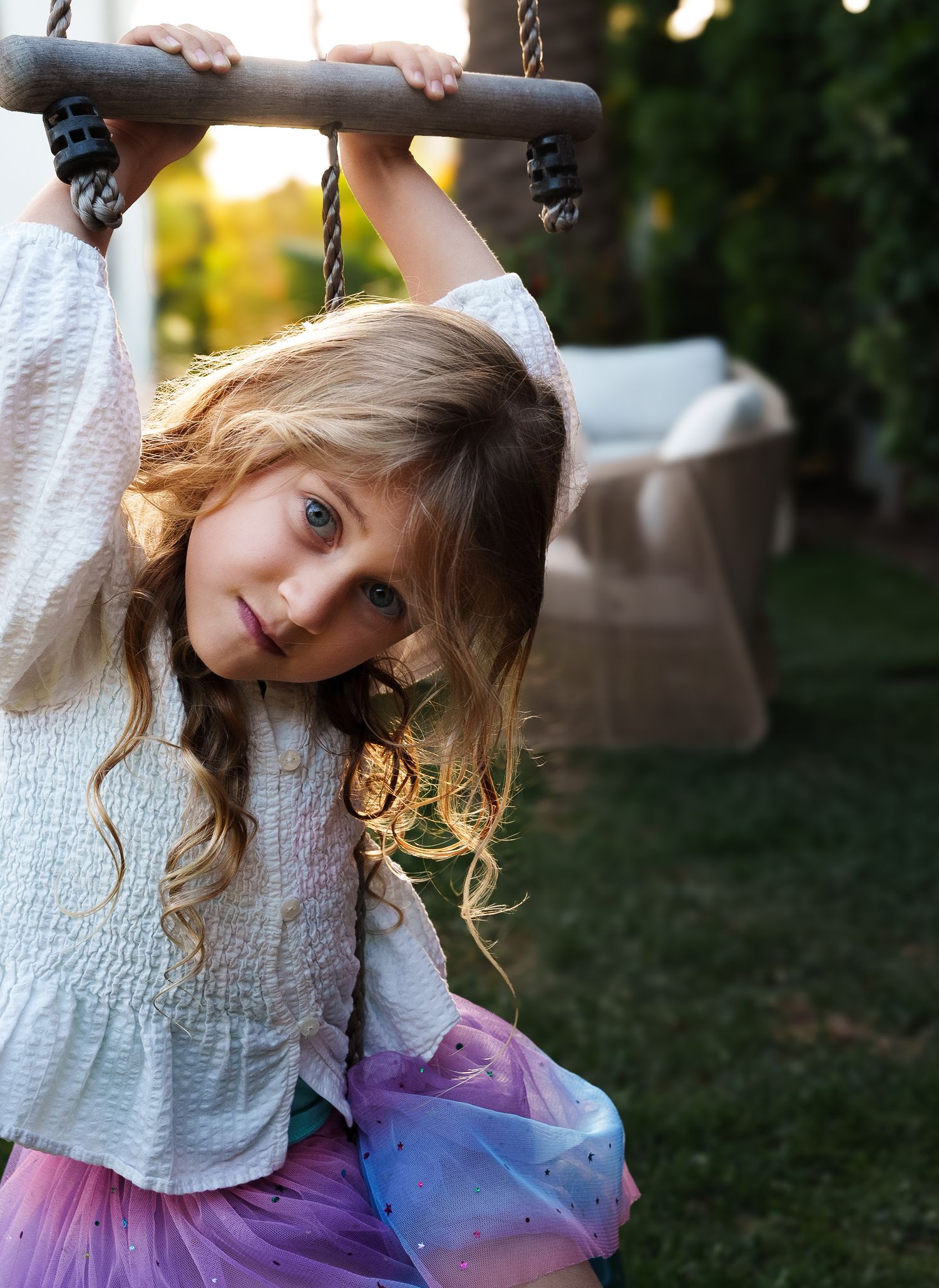 a young girl hanging from a bar in her backyard looking directly at the camera