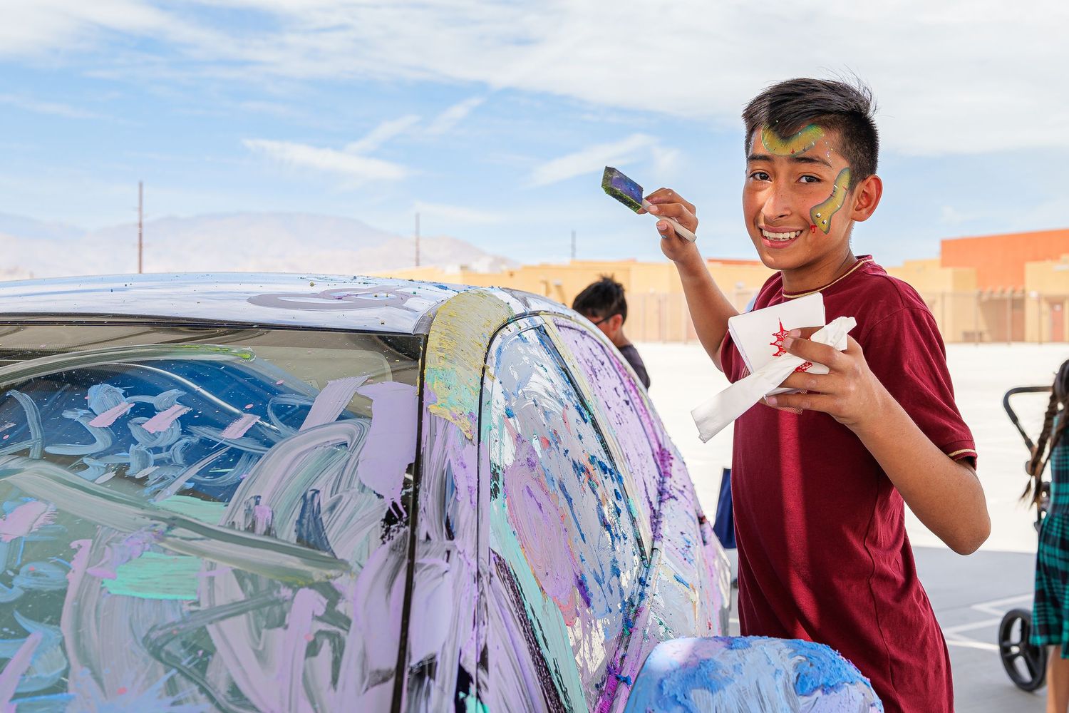 A group of people paint a large colorful mural on a wall outdoors during a community art project.