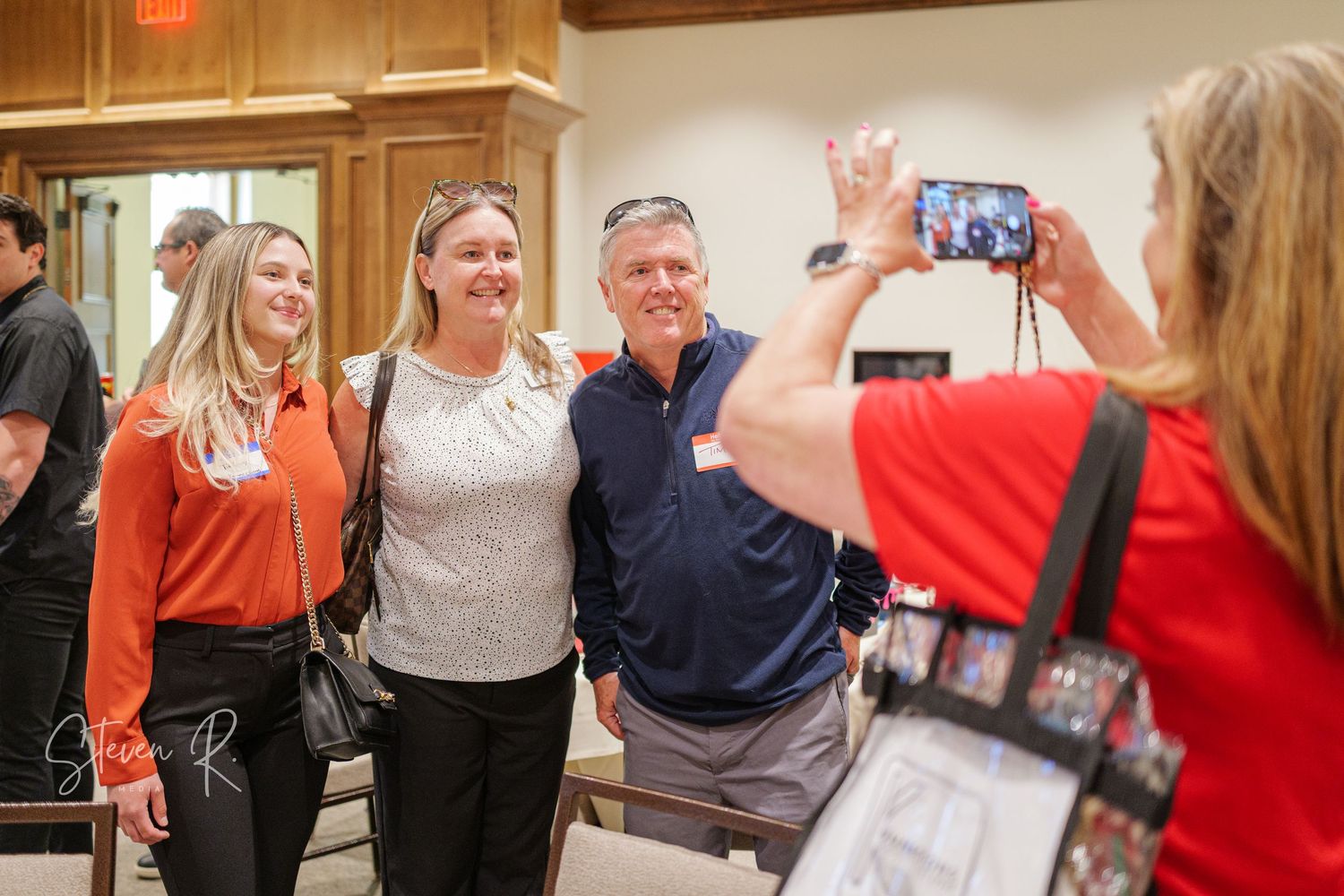 A group of people celebrate and raise their arms in excitement inside a wood-paneled room.