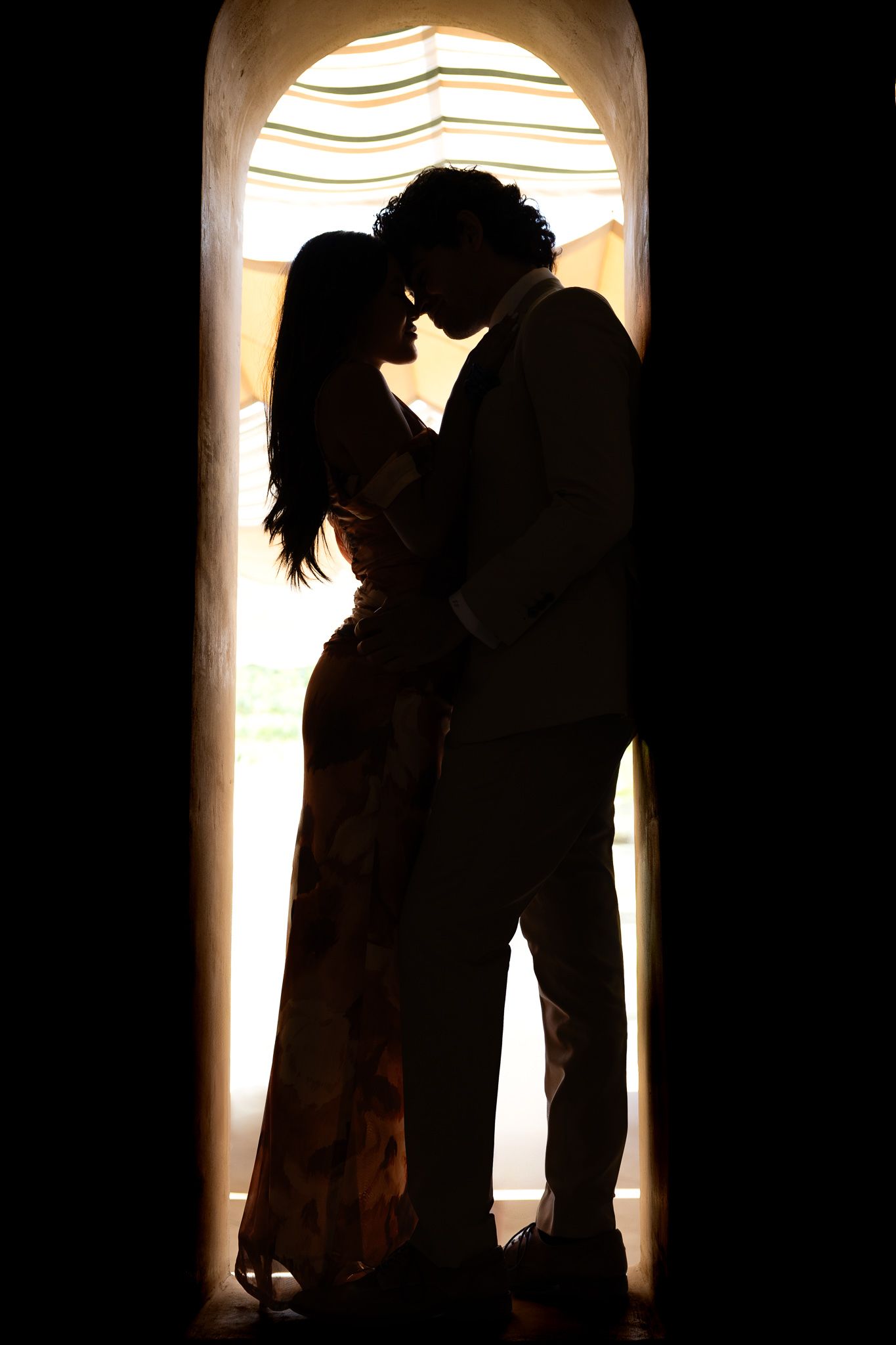 Romantic silhouettes against backlit windows show a couple embracing in dramatic lighting. Artistic portraits. Engagement photos.