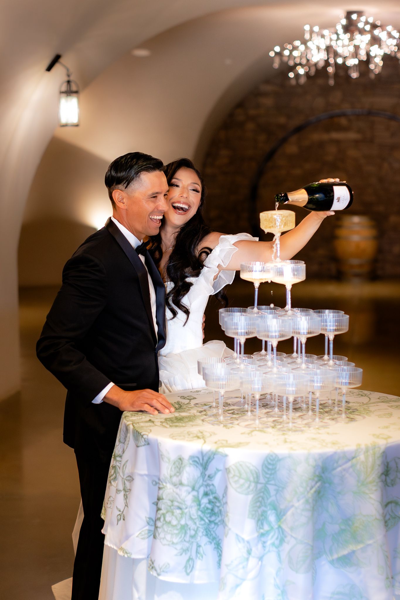 A couple pouring champagne into a tower of glasses at their wedding reception in a luxury winery. Happiness and elegance.