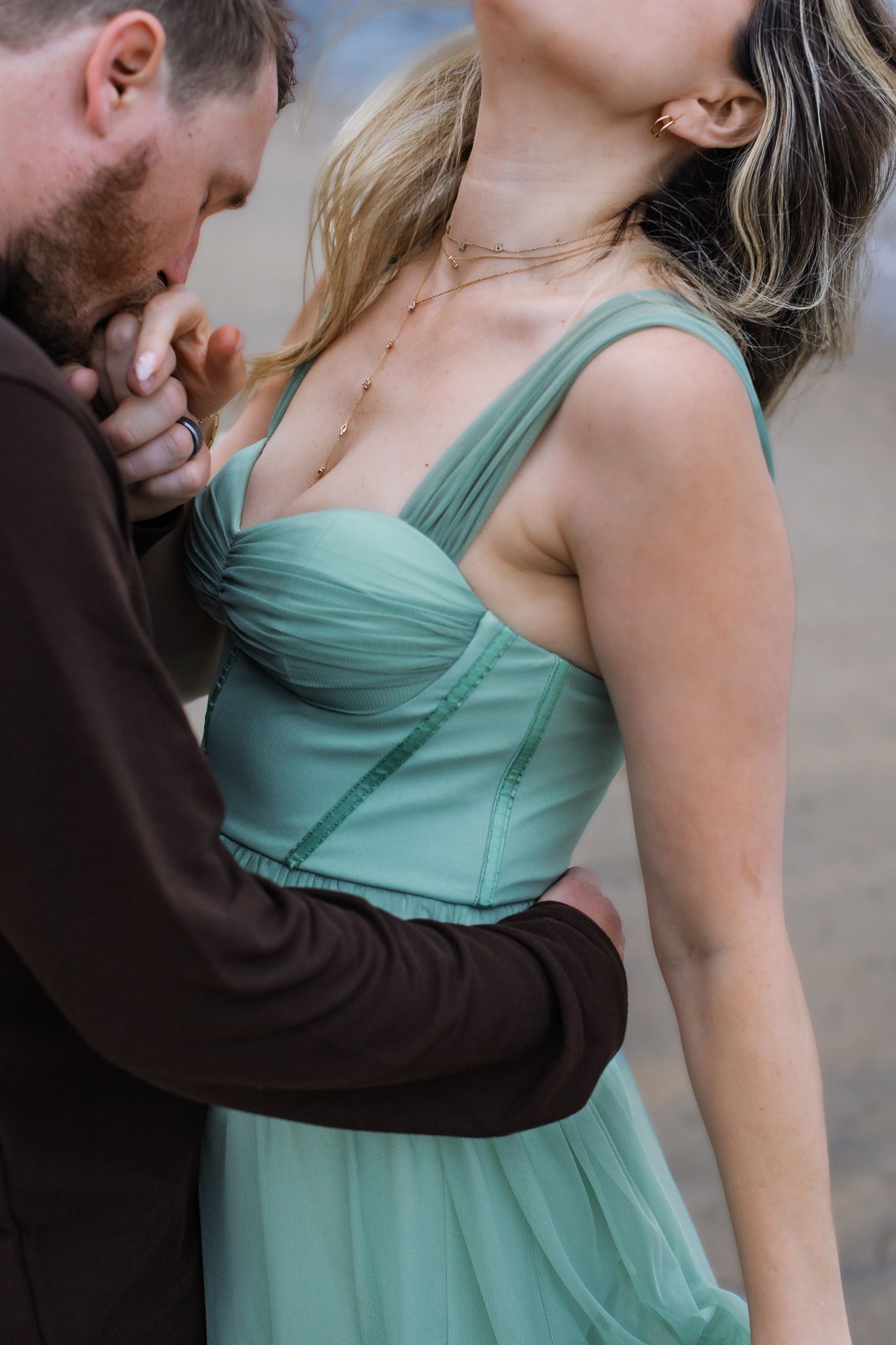 A romantic couple embraces intimately, with her wearing a mint green formal dress and him in a dark sweater. Engagement photos in San Diego.