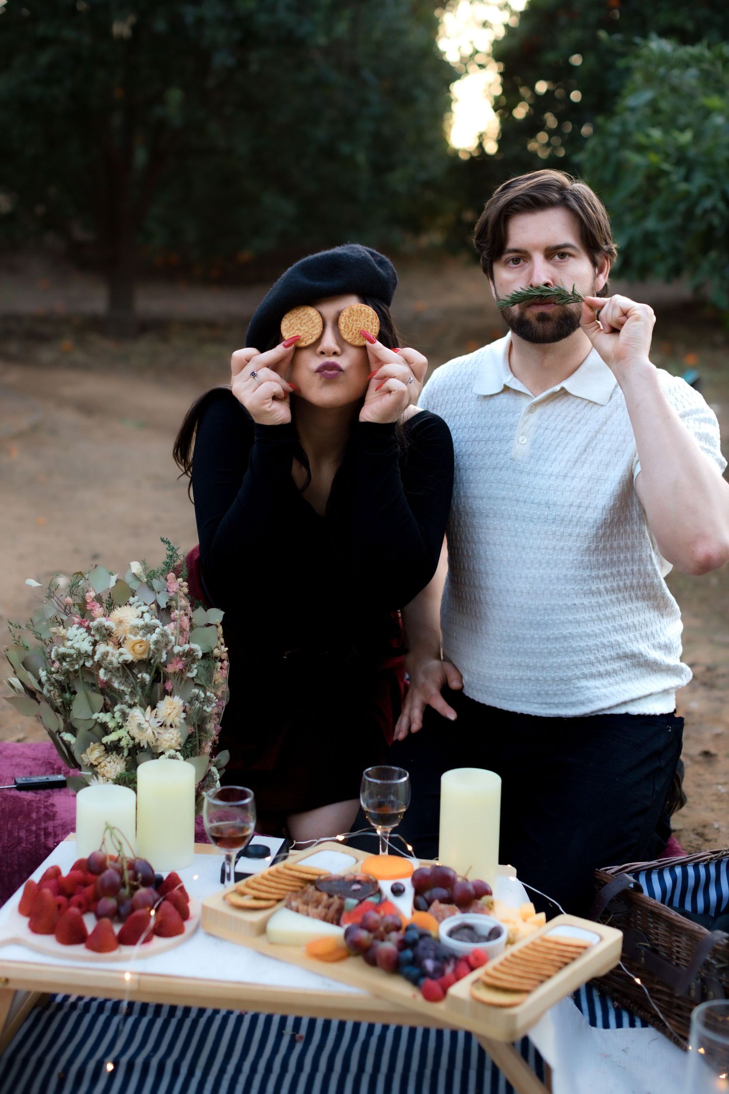 Couple having fun at outdoor picnic with charcuterie board, fruits, and candles at sunset. Engagement photos. Engaged couples. Fun and cute.