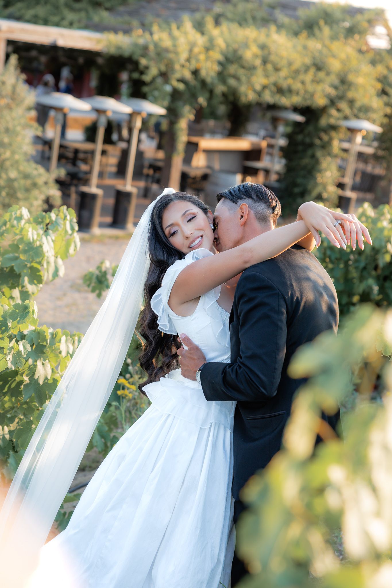 Bride and Groom in a romantic embrace in a garden setting with sunlit foliage. Golden hour portraits. Wedding photos. Elegant couple.