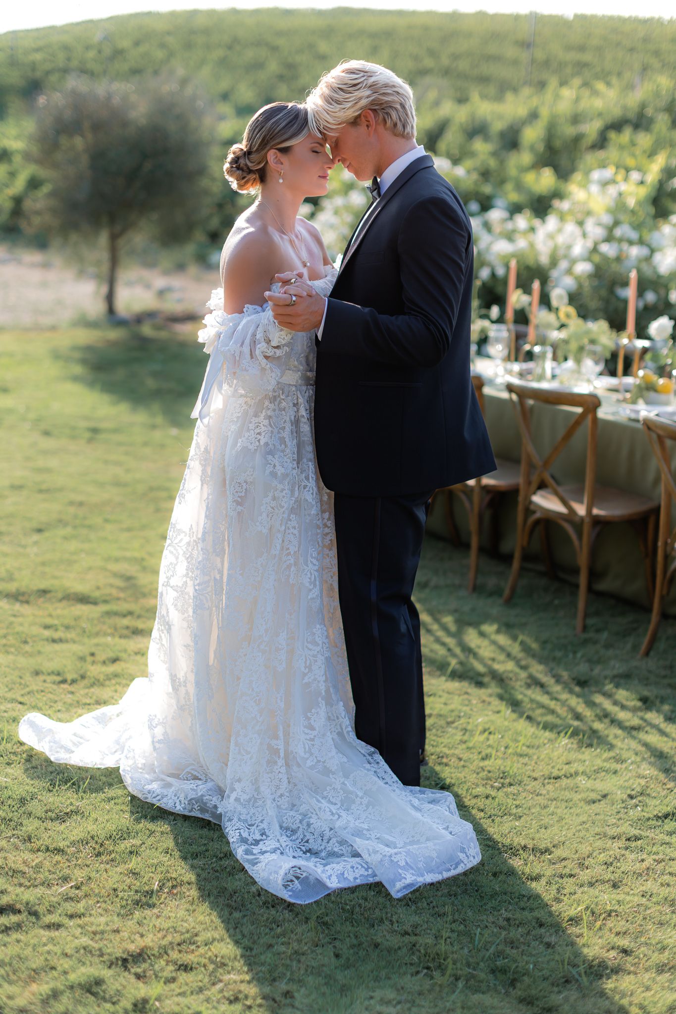 A romantic outdoor wedding scene with a couple embracing on a grassy lawn during golden hour. Couples first dance as husband and wife.
