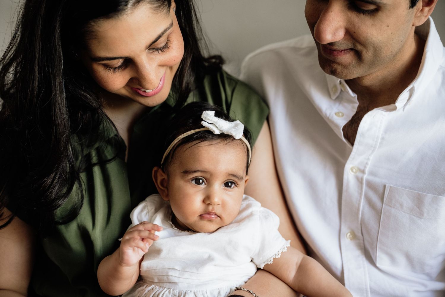 Sweet family portrait session showing parents lovingly interacting with their baby in white outfits.