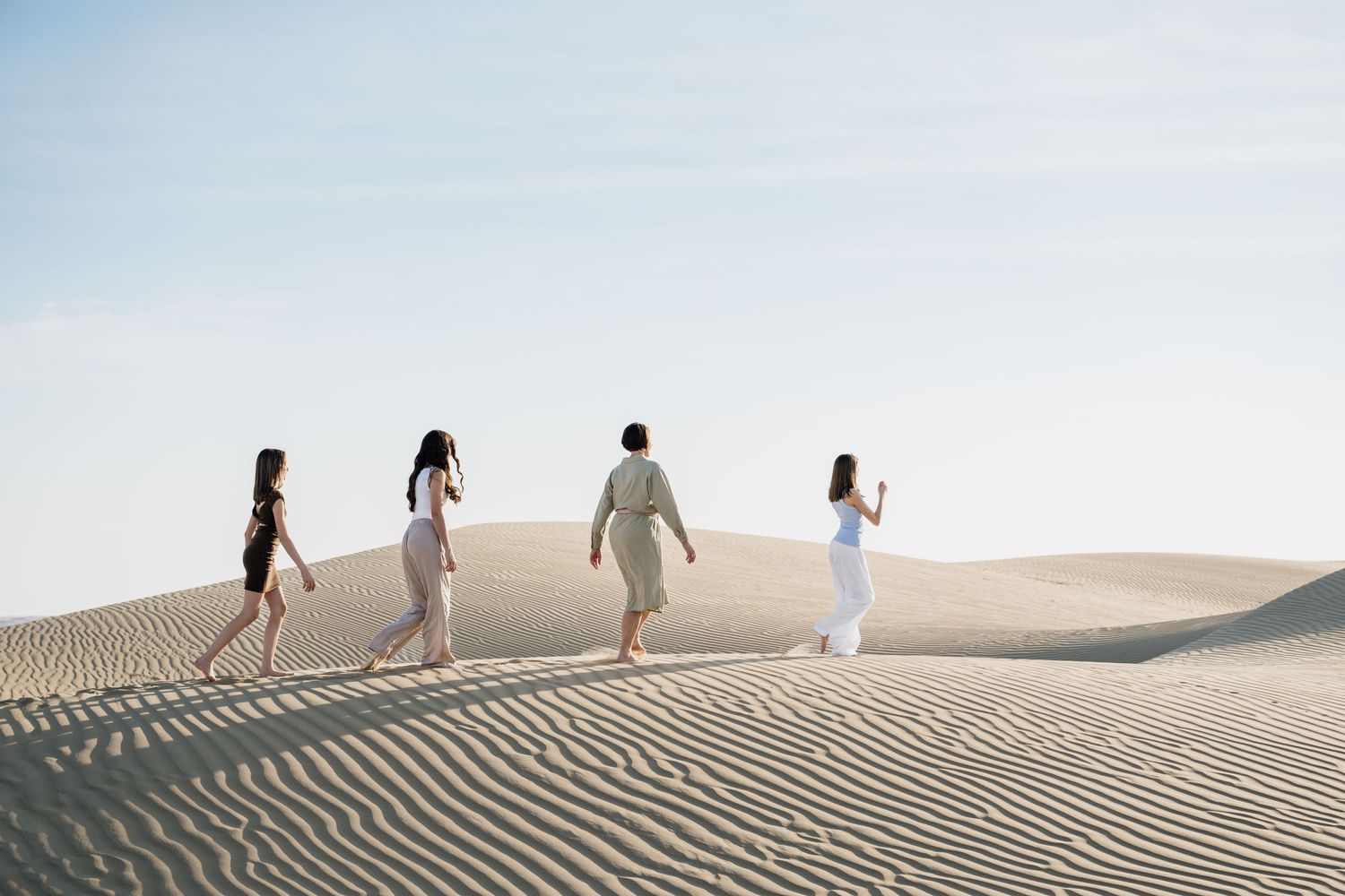 Silhouettes of people walking along sand dune ridges at sunset.