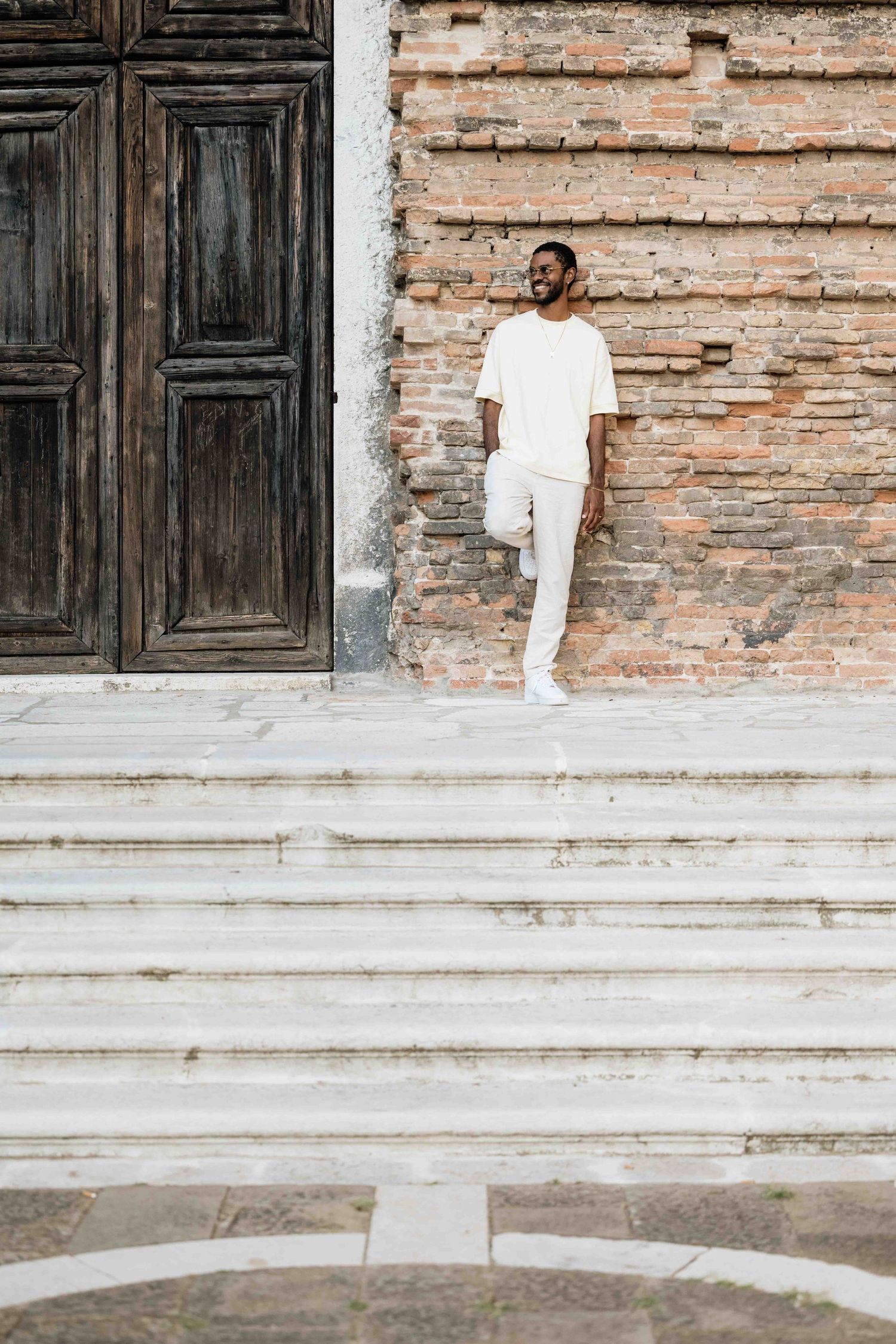 Person in white clothing photographed sitting on outdoor stone steps near brick building.