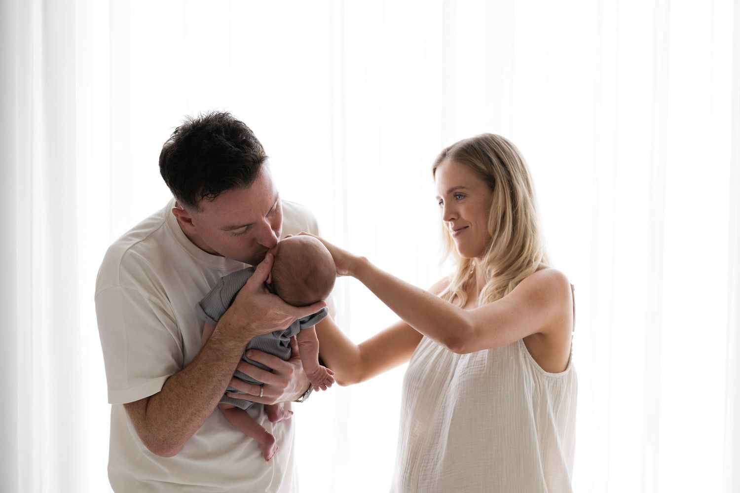 Photo of father cuddling a baby with mother arranging his outfit
