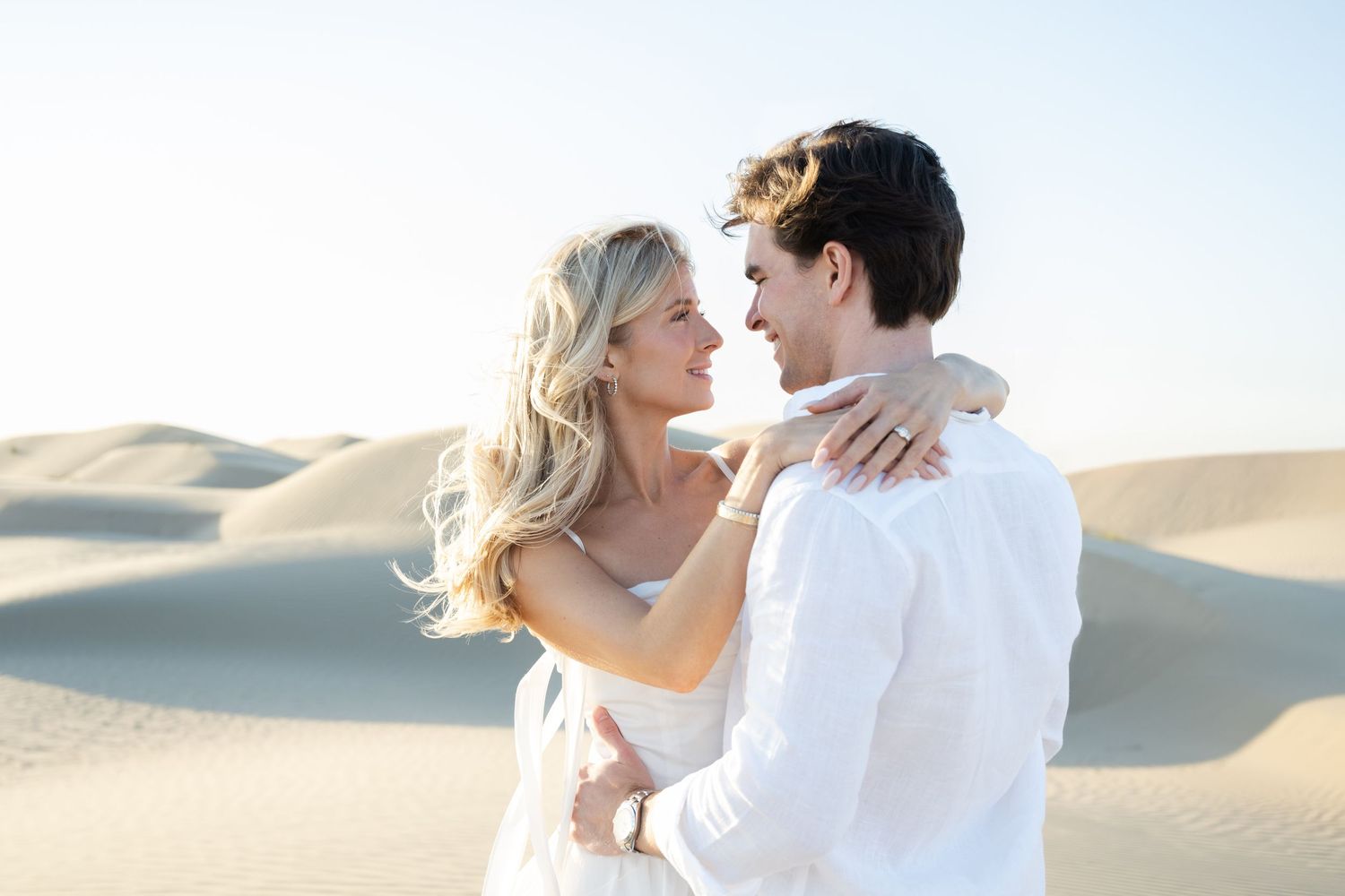 Romantic couple embracing on sand dunes during sunset photoshoot.