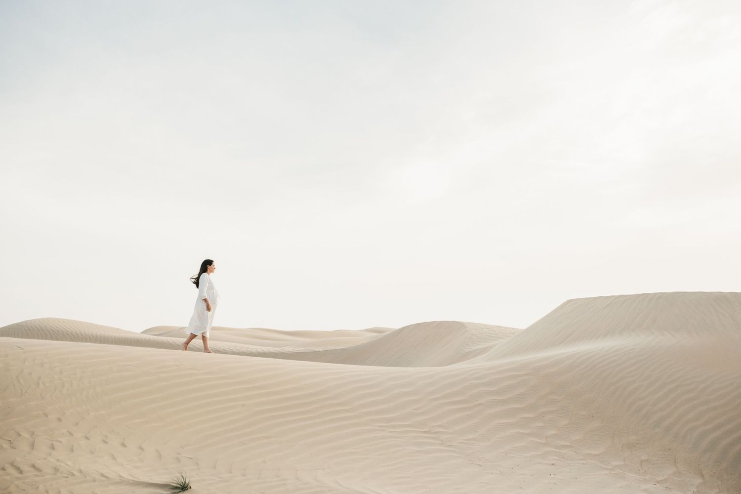 Distant view of couple standing on vast desert sand dunes under bright sky.