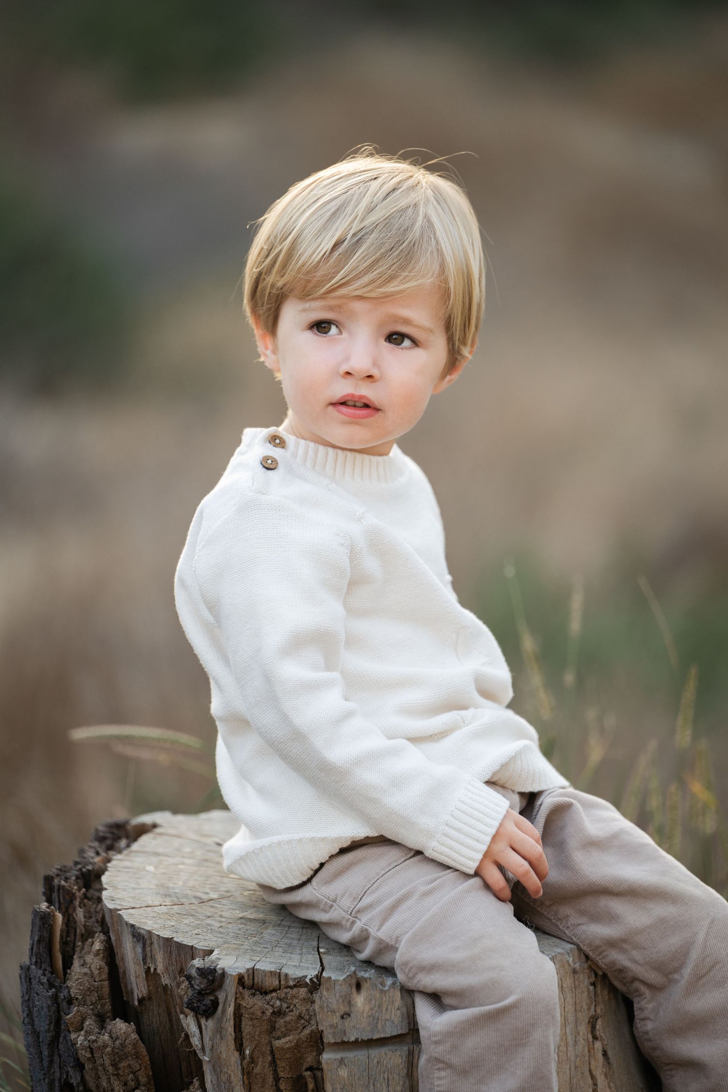 Child portrait series on rustic wood stump in white sweater against natural background.